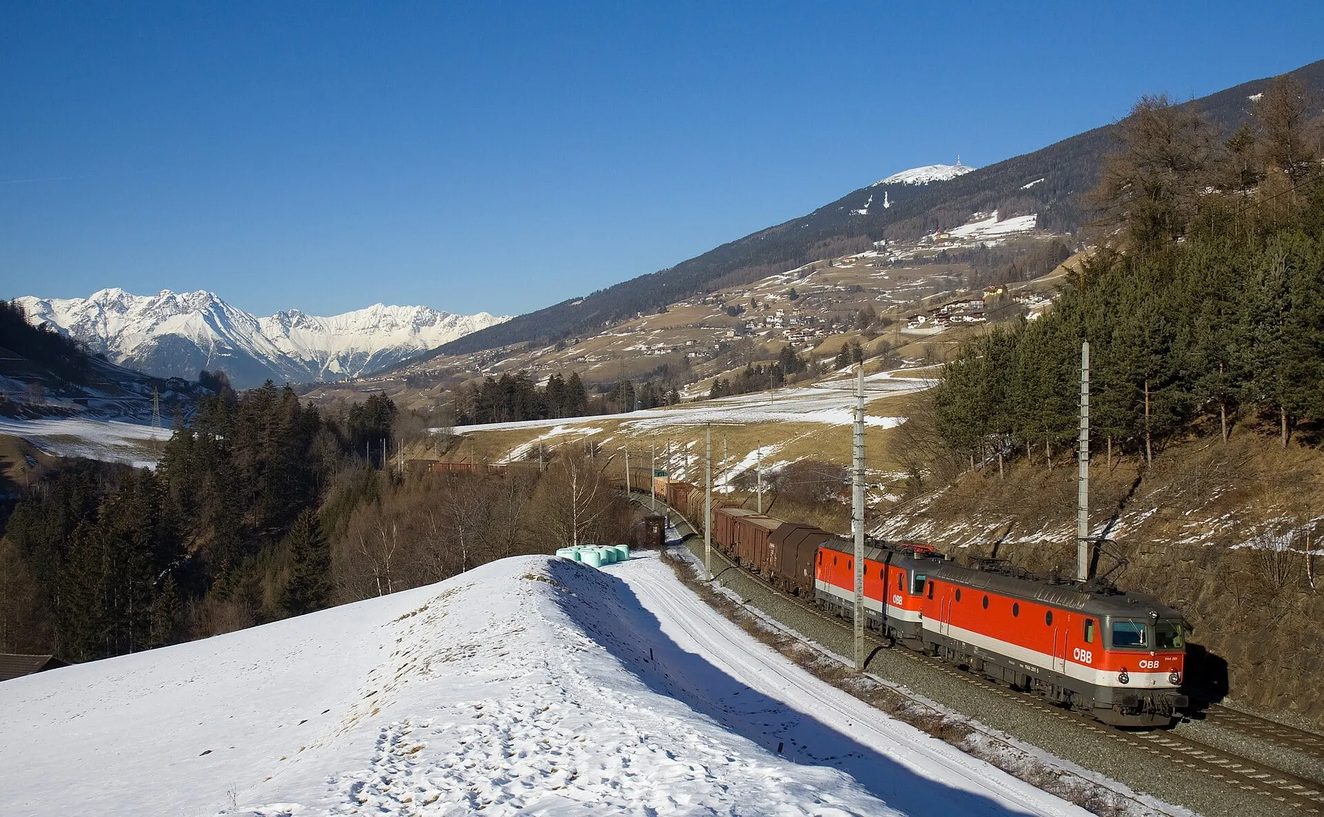 A freight train with two red ÖBB locomotives on the Brenner railway between Innsbruck and Matrei, with snowy peaks behind