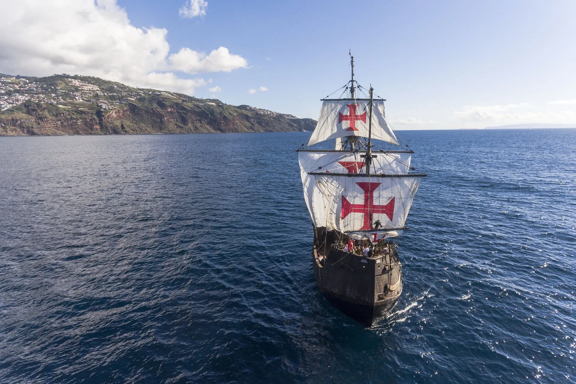 The ship seen from ahead, sails set, with the cliffs of the south coast to the west of Funchal on the left