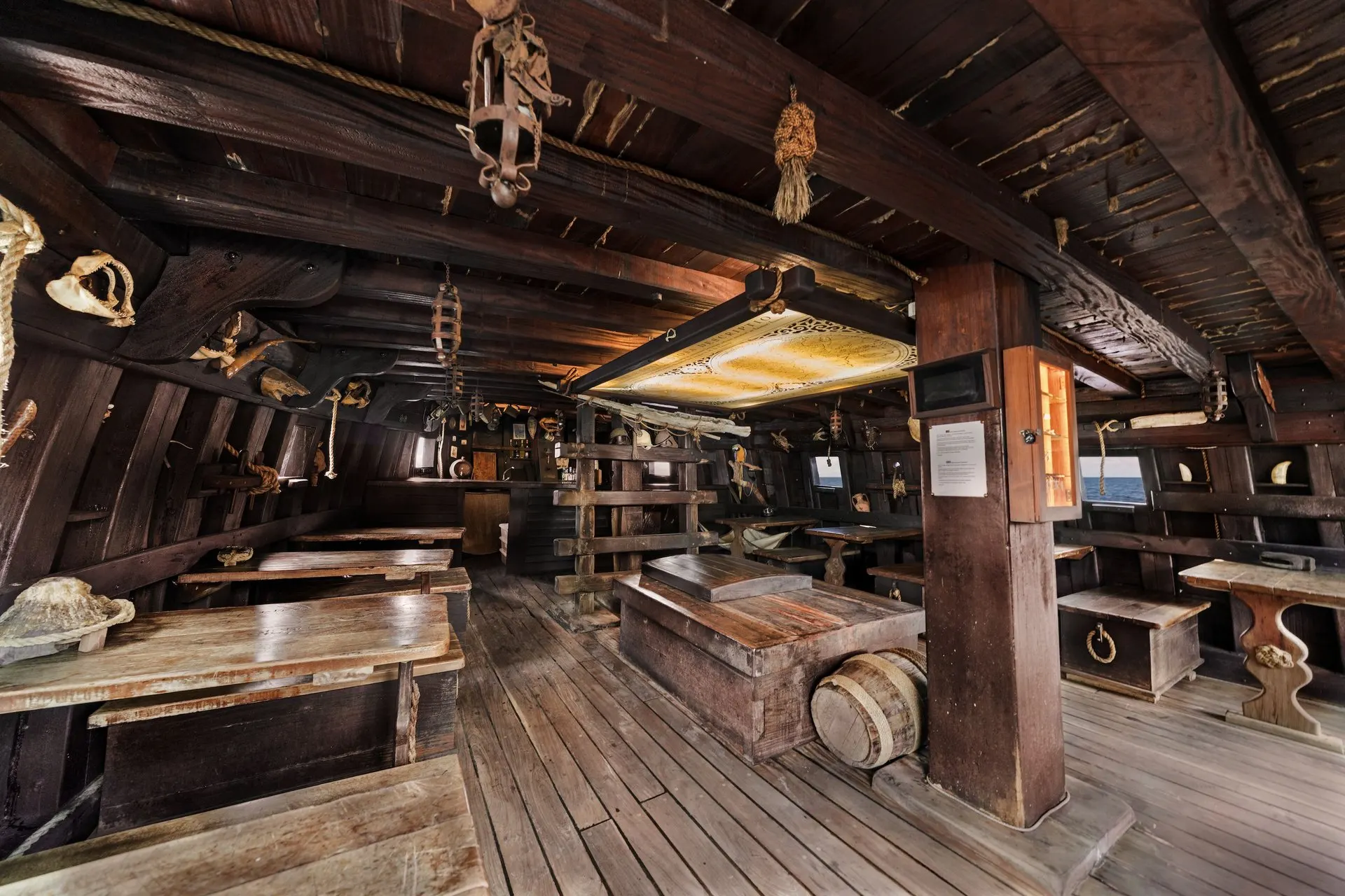 The lower deck: wooden tables and benches, ropes, lanterns and a painted map overhead