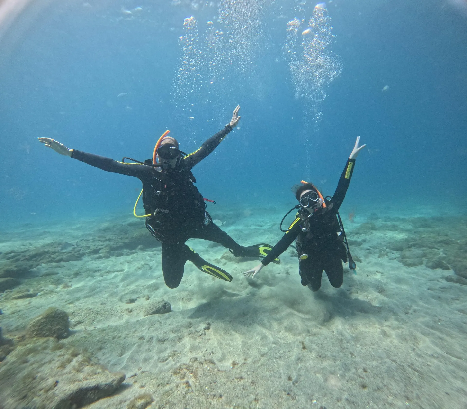 Two divers raising their arms over a sandy seabed