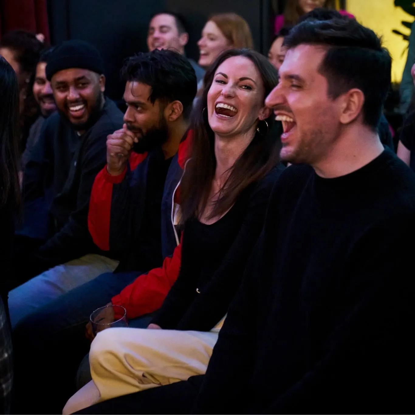 Audience members in a row of seats laughing at a comedy show
