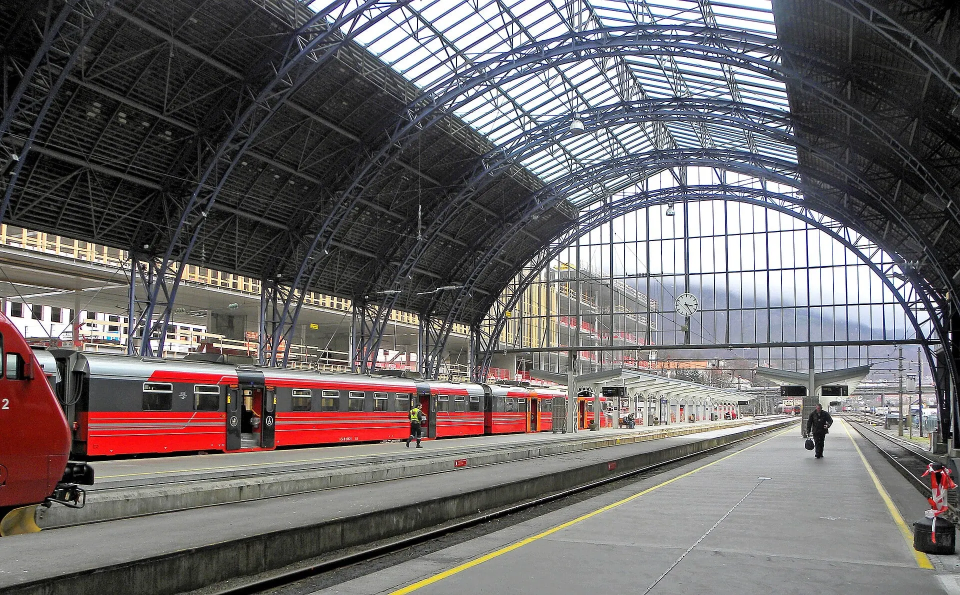 Red trains under the arched glass roof of the train hall at Bergen station.