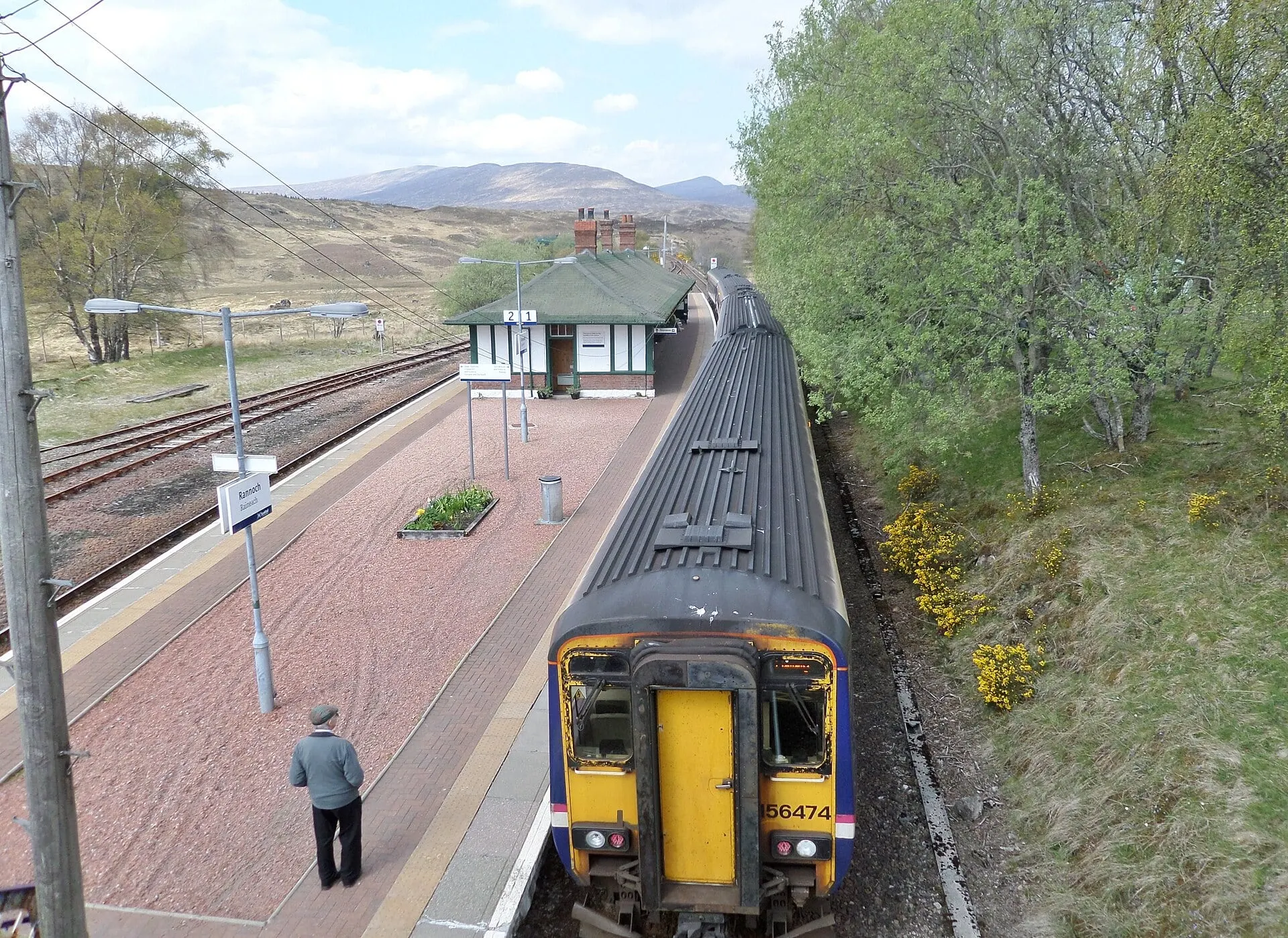 A ScotRail train at Rannoch station, with its chalet style station building and the open moor behind.