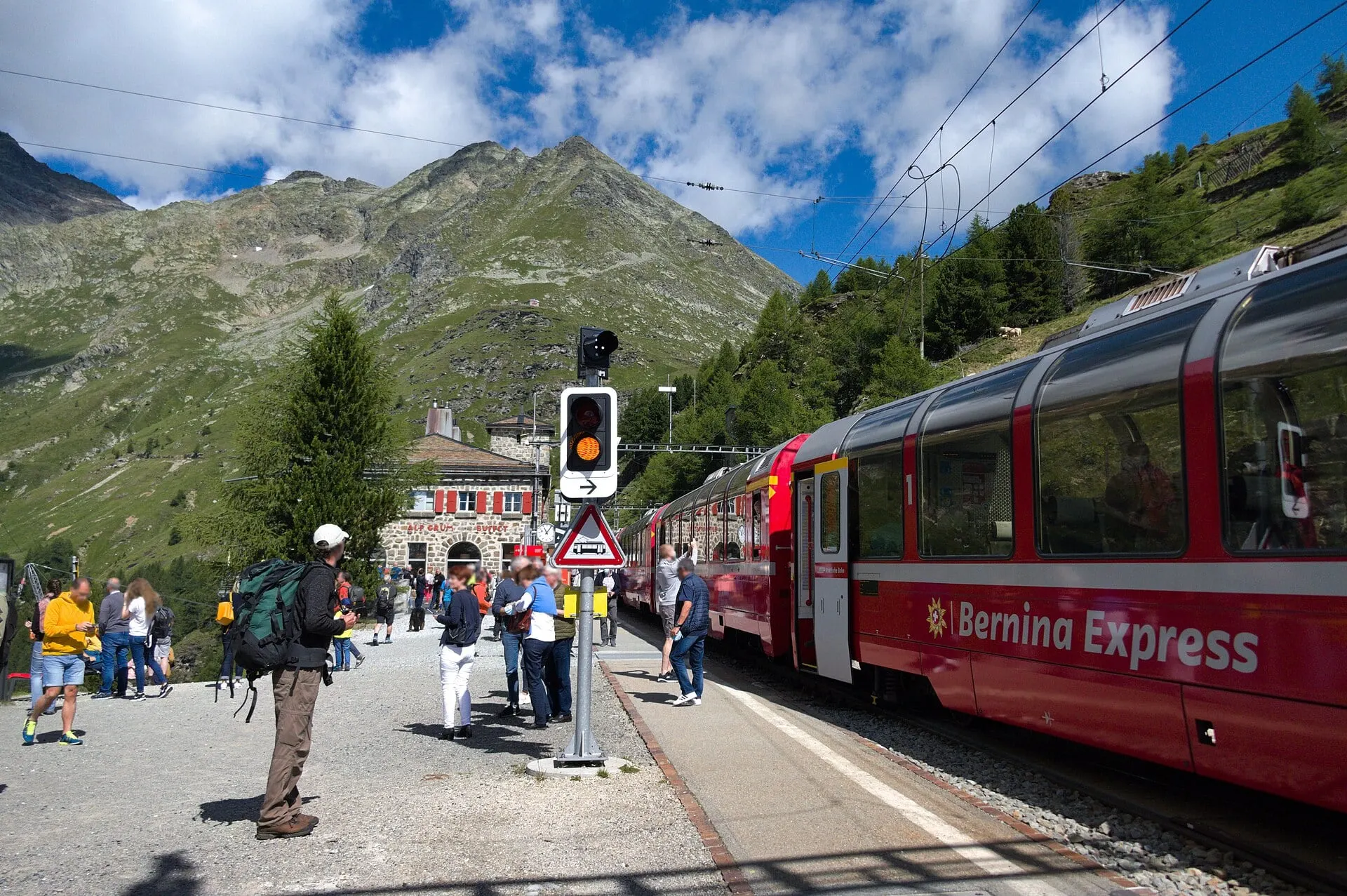 The Bernina Express standing at Alp Grüm station in front of the stone station building.