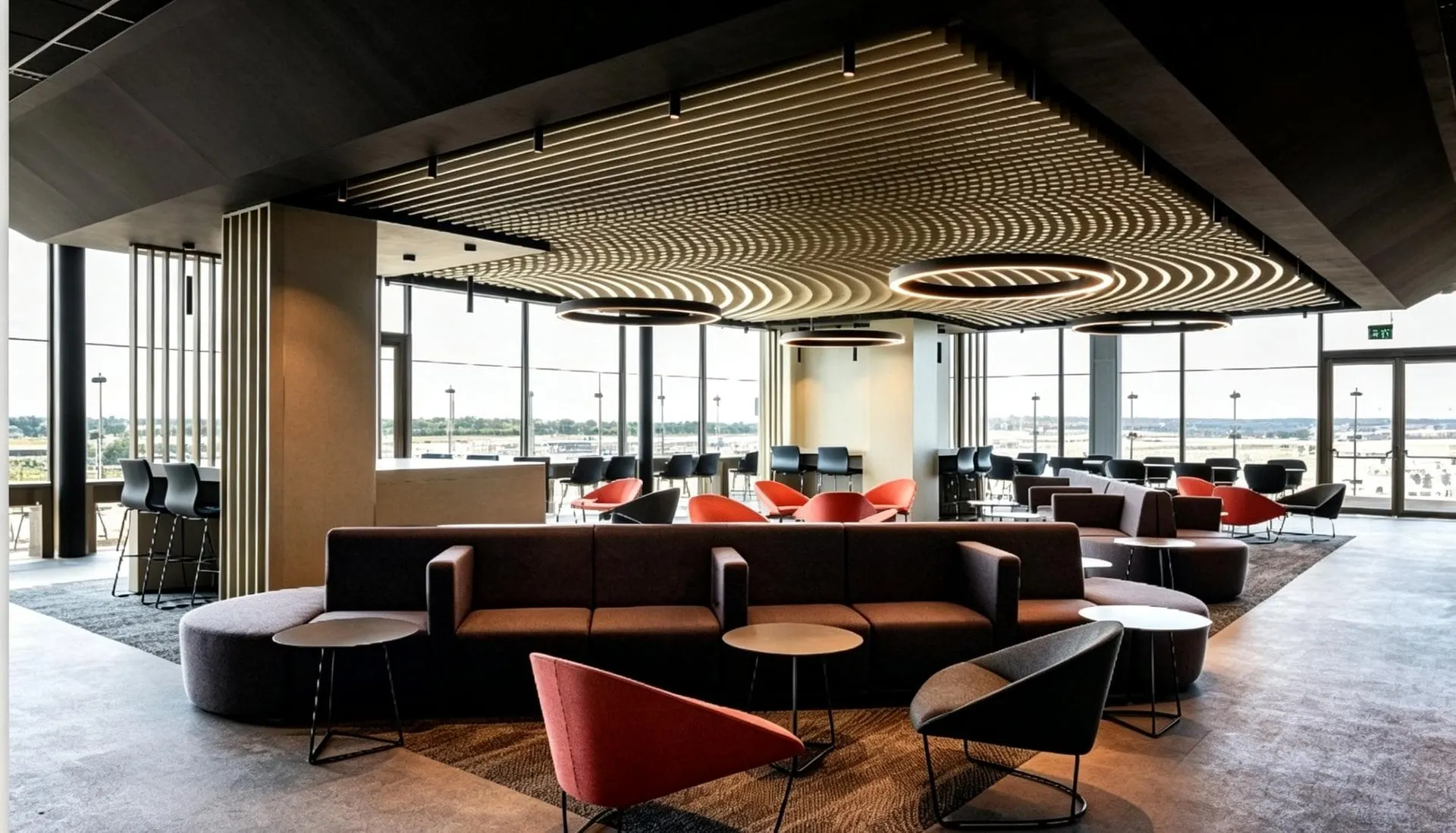Open lounge with low sofas, red armchairs and a circular ceiling light by tall windows