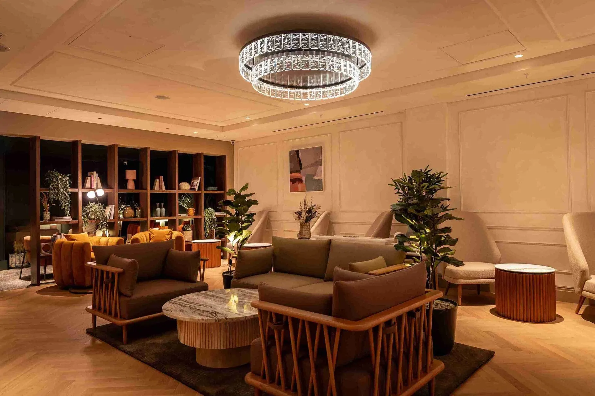 Sofas and armchairs around low tables under a crystal chandelier, with plants and bookshelves behind
