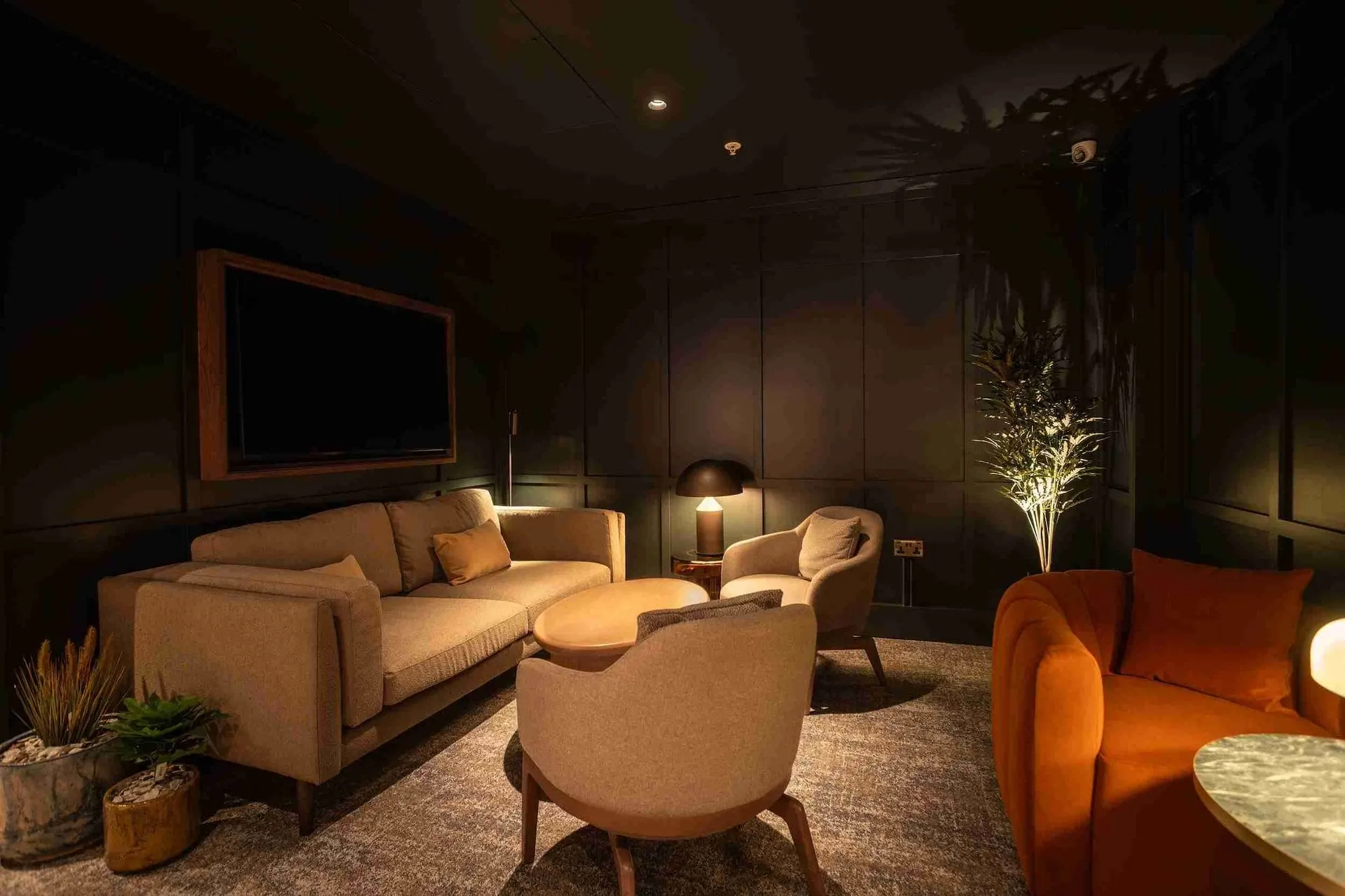 Cream sofa and armchairs beneath a wall-mounted TV in a dimly lit corner