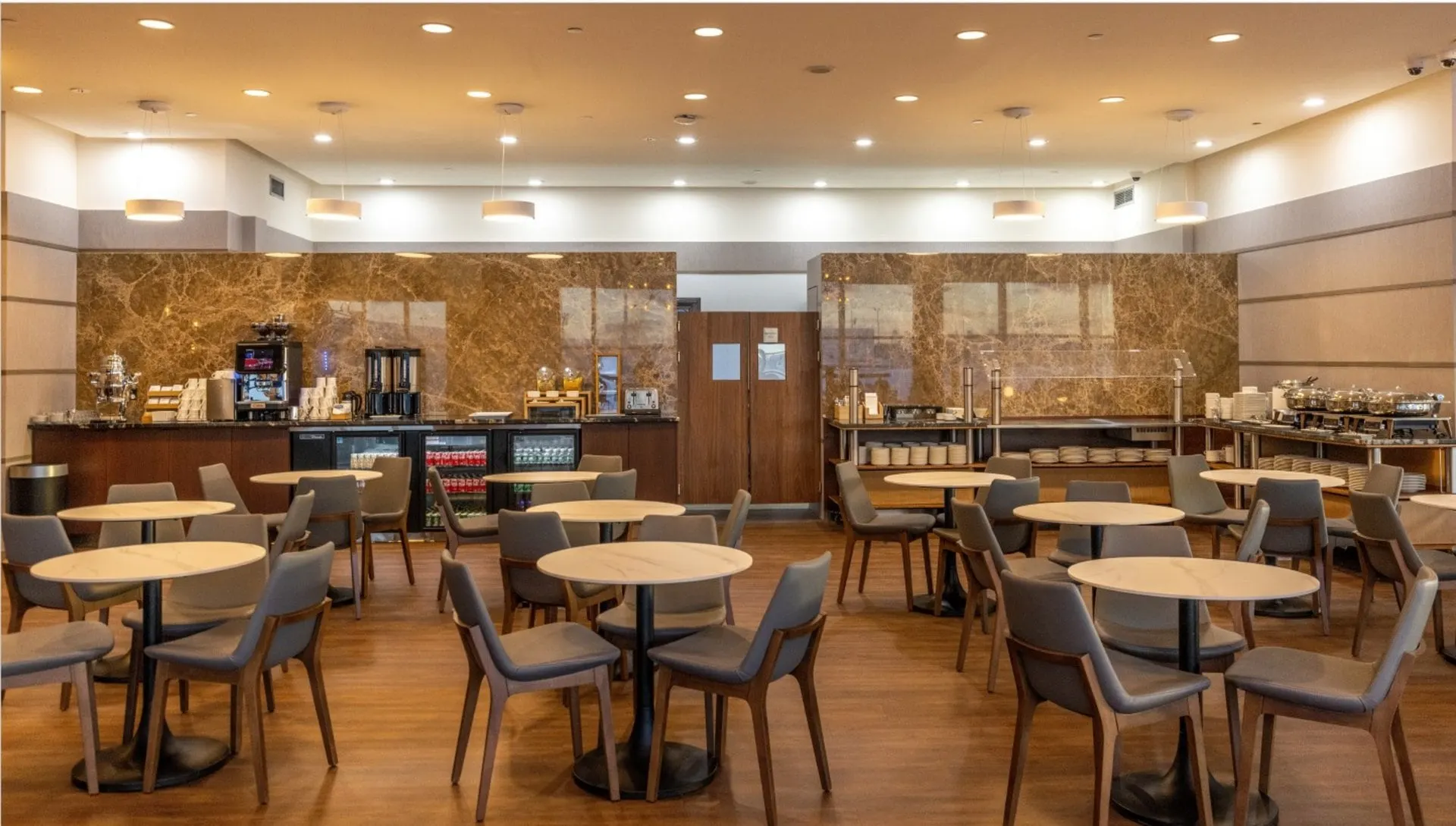 Dining area with round tables and grey chairs in front of a marble-backed buffet counter