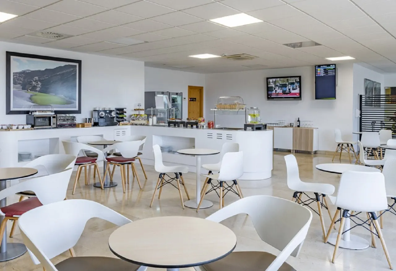 Self-service counter with coffee machine and drinks fridges behind white chairs and round tables