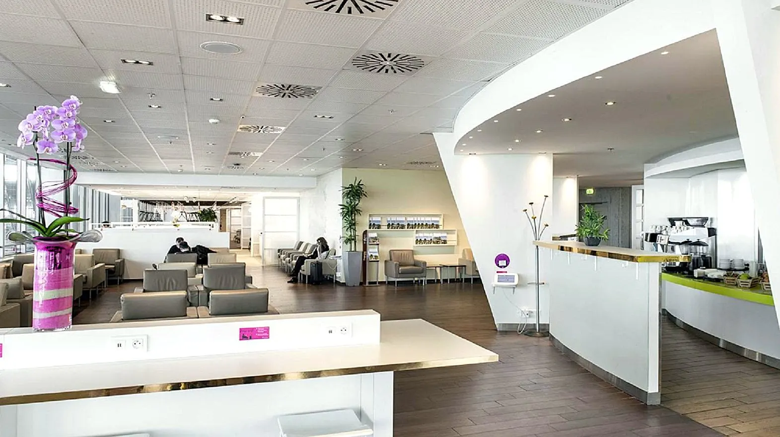 White lounge with grey armchairs, a long counter and seating beyond