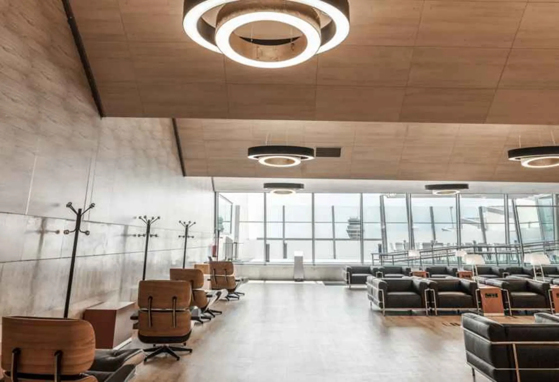 Fauteuils et canapés en cuir face à une longue paroi vitrée sous des luminaires en anneau