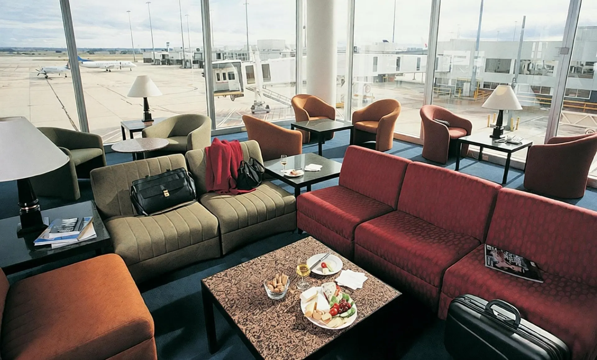 Red and grey sofas with table lamps beside floor-to-ceiling windows over the apron at Porto Airport