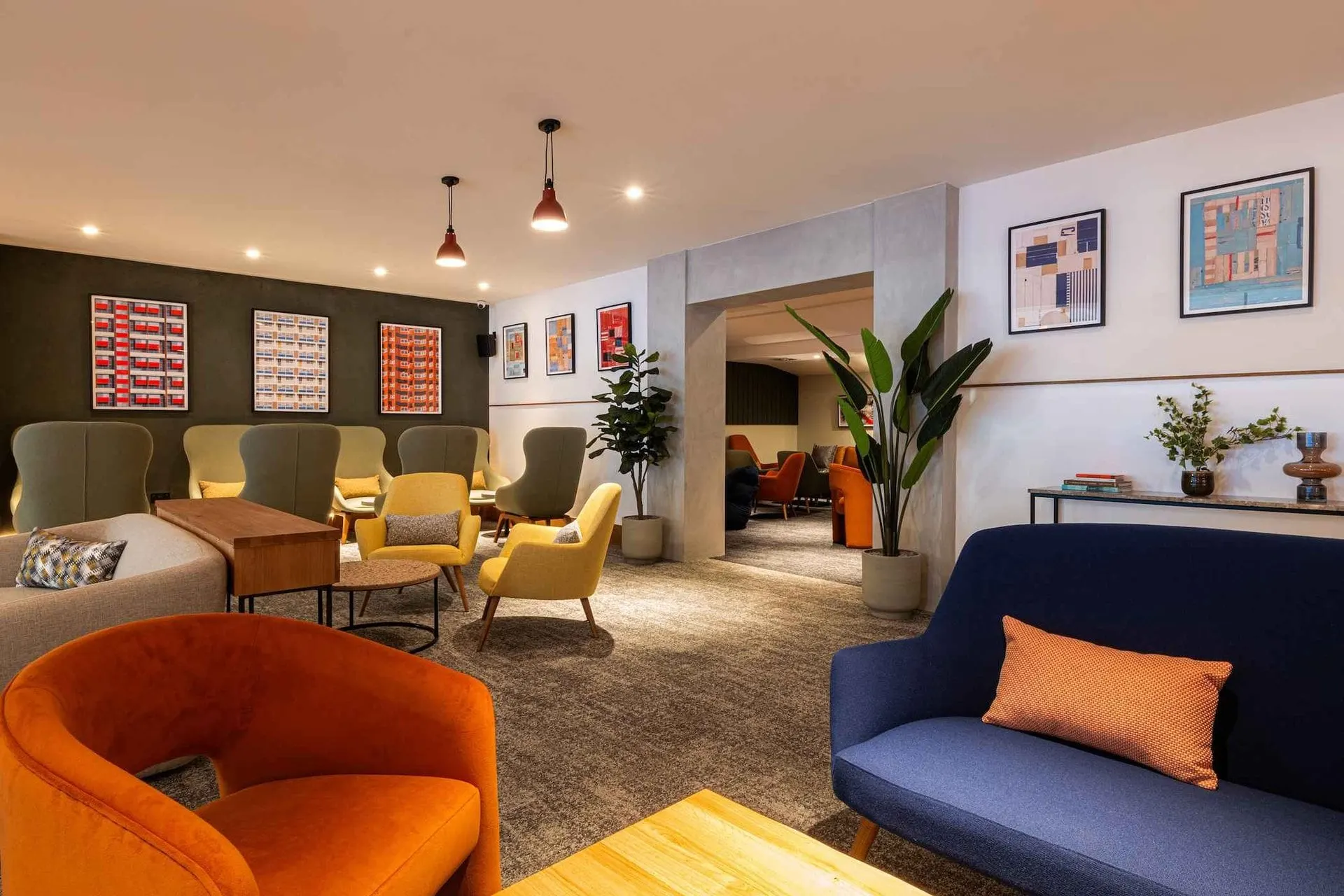 Navy sofa with an orange cushion, armchairs and framed prints on the walls
