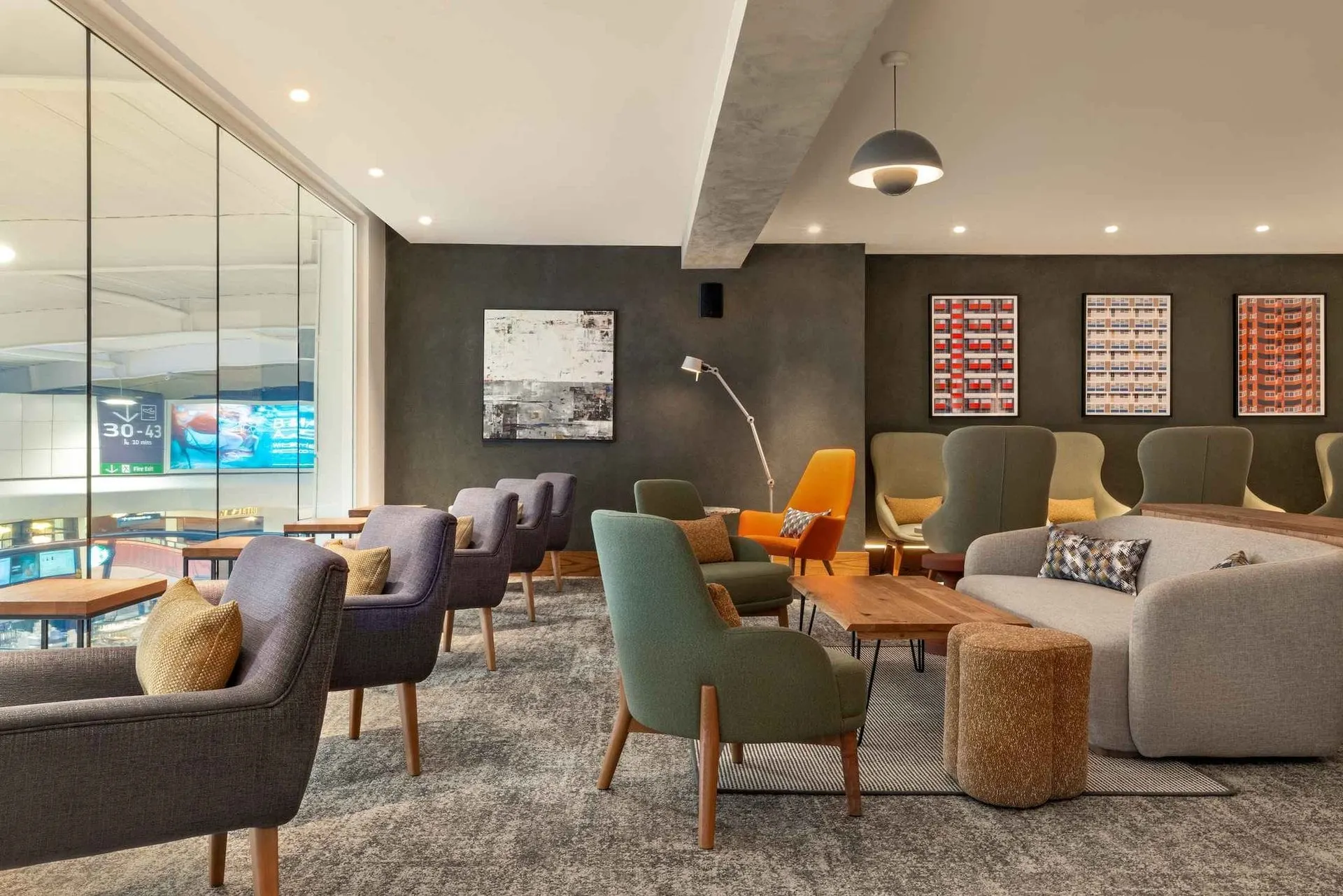 Grey and green armchairs around low wooden tables beside a glass-walled room