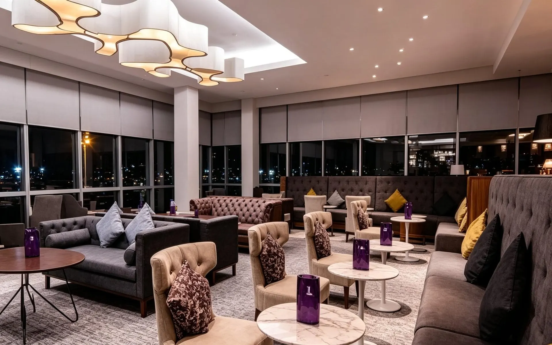 Grey sofas, armchairs and cushions under sculpted ceiling lights in front of large windows