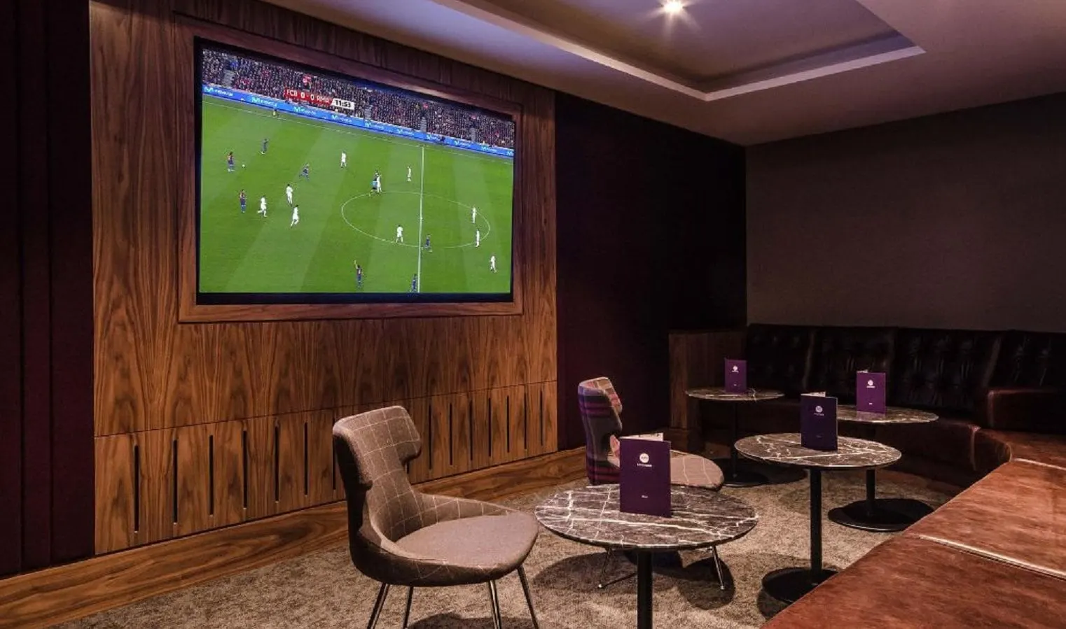 TV room with a big screen showing football, wood panelling and small tables