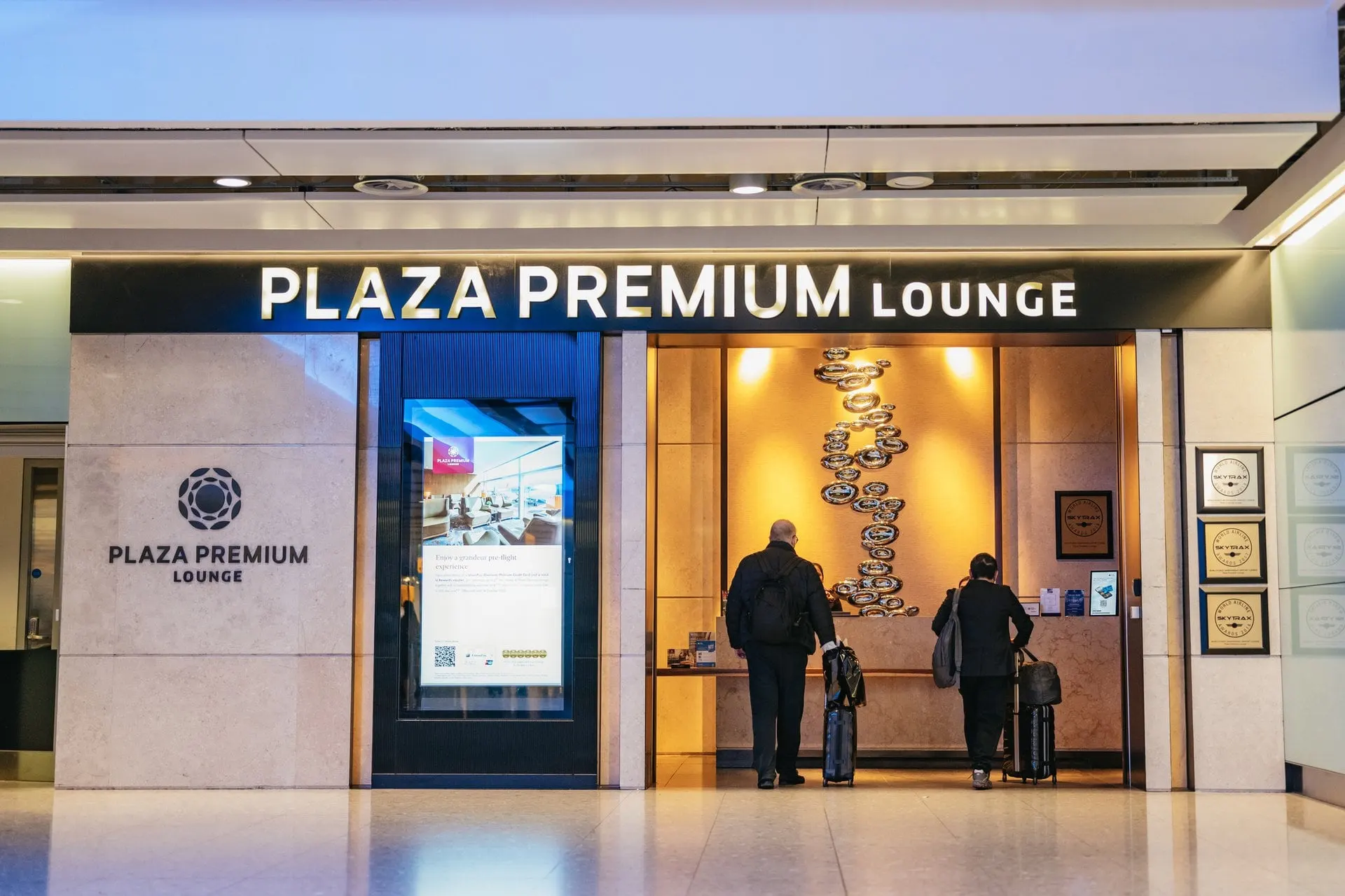 Entrance to the Plaza Premium Lounge in a Heathrow terminal, with travellers at the desk