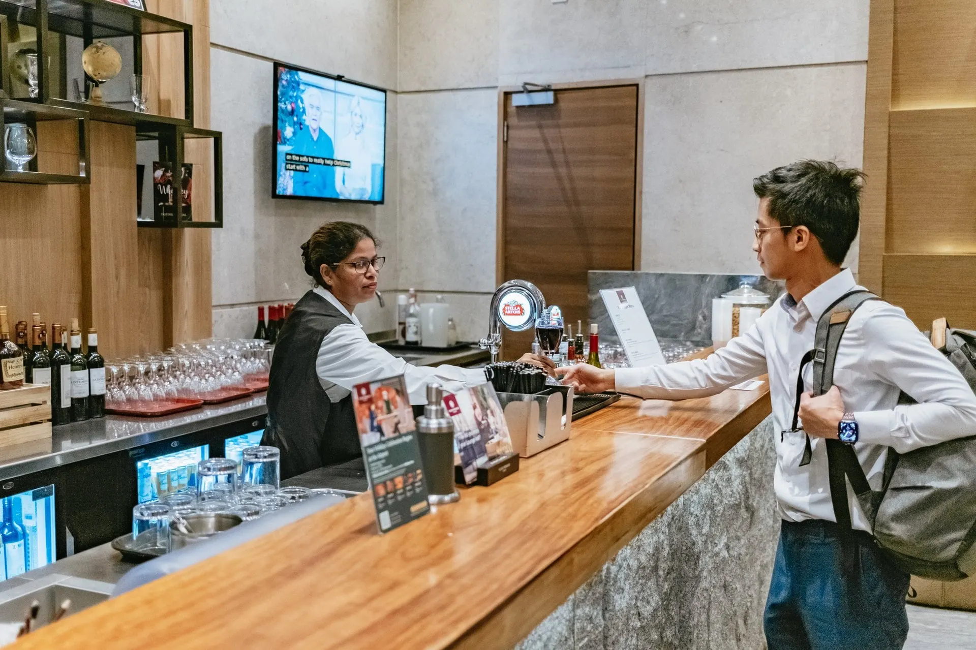 Bartender handing a drink across a wooden bar counter to a traveller with a backpack