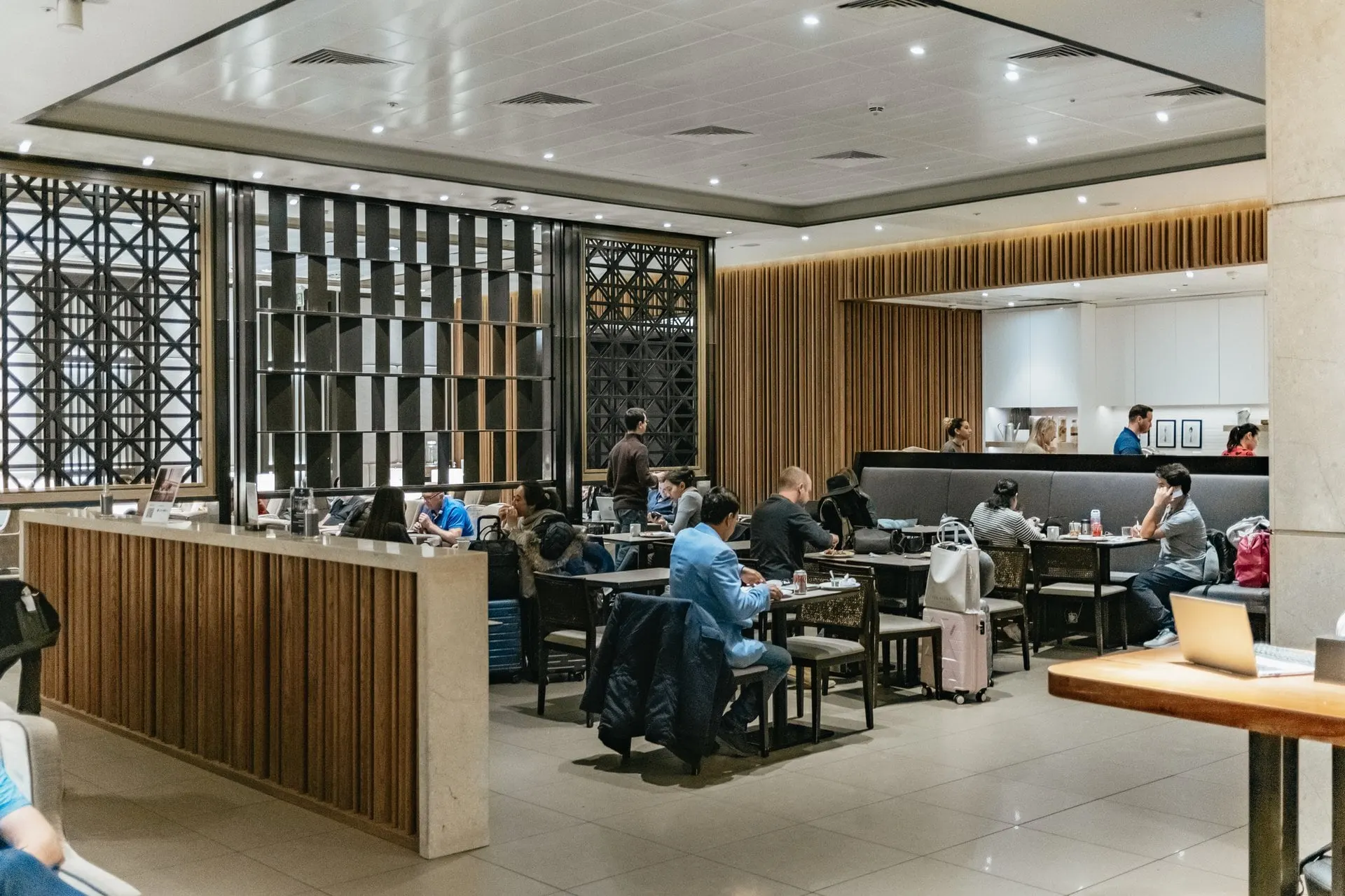 Dining area with dark tables and chairs behind a carved wooden screen, guests eating and working