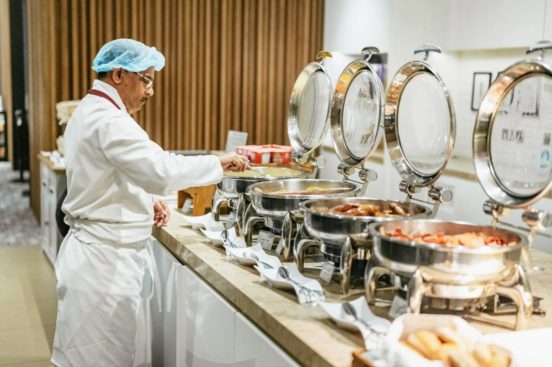 Chef in whites serving from a row of silver chafing dishes at the hot buffet
