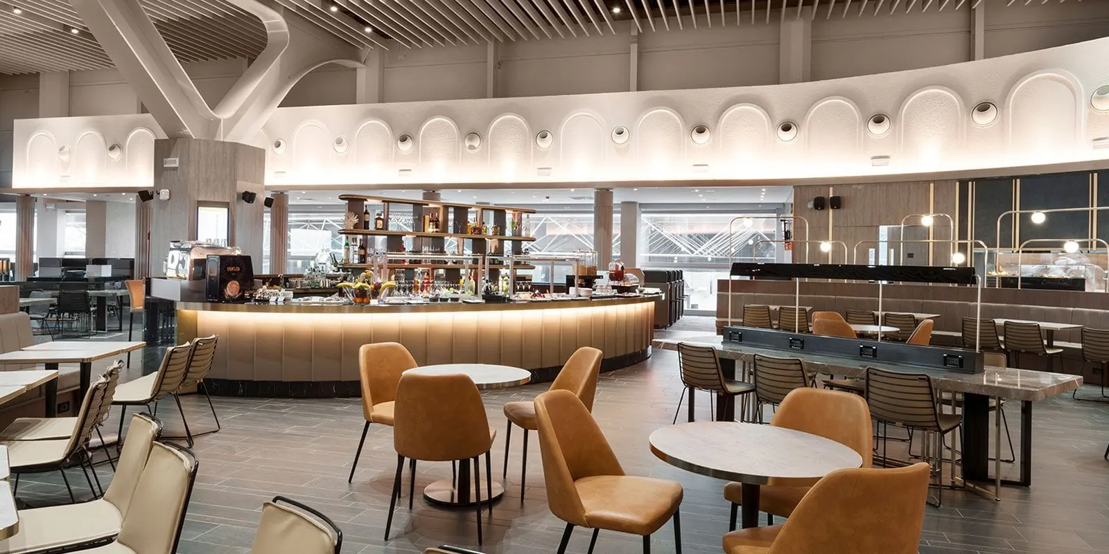 Curved buffet and drinks counter with leather chairs and round marble tables