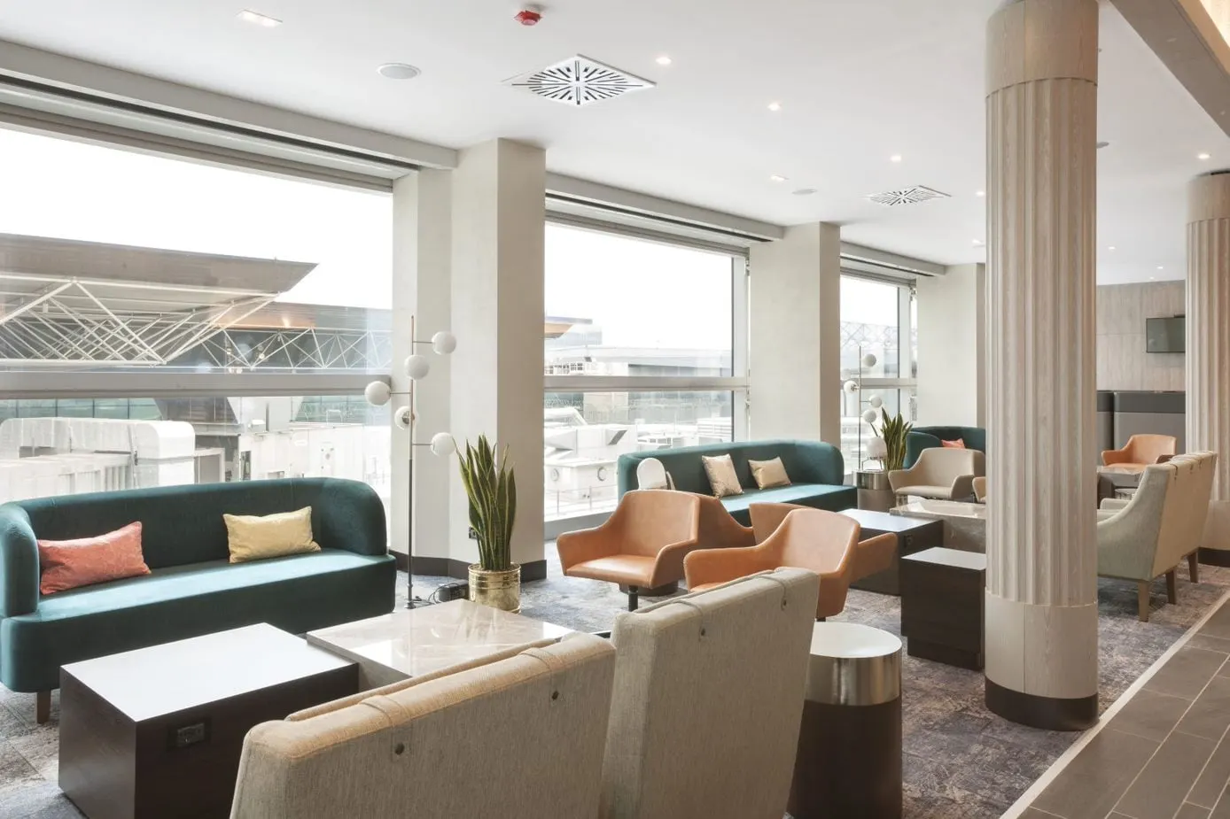 Teal sofa with orange cushions, armchairs and a plant by windows onto the airfield