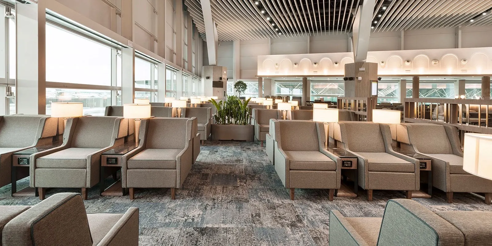 Rows of beige armchairs with side tables under a slatted ceiling and arched lights