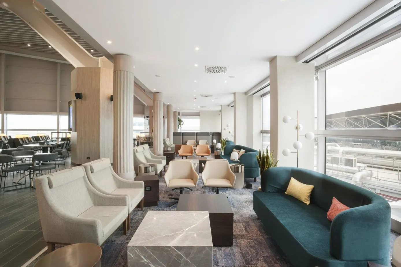 Cream armchairs and a teal sofa around a marble table beside large windows