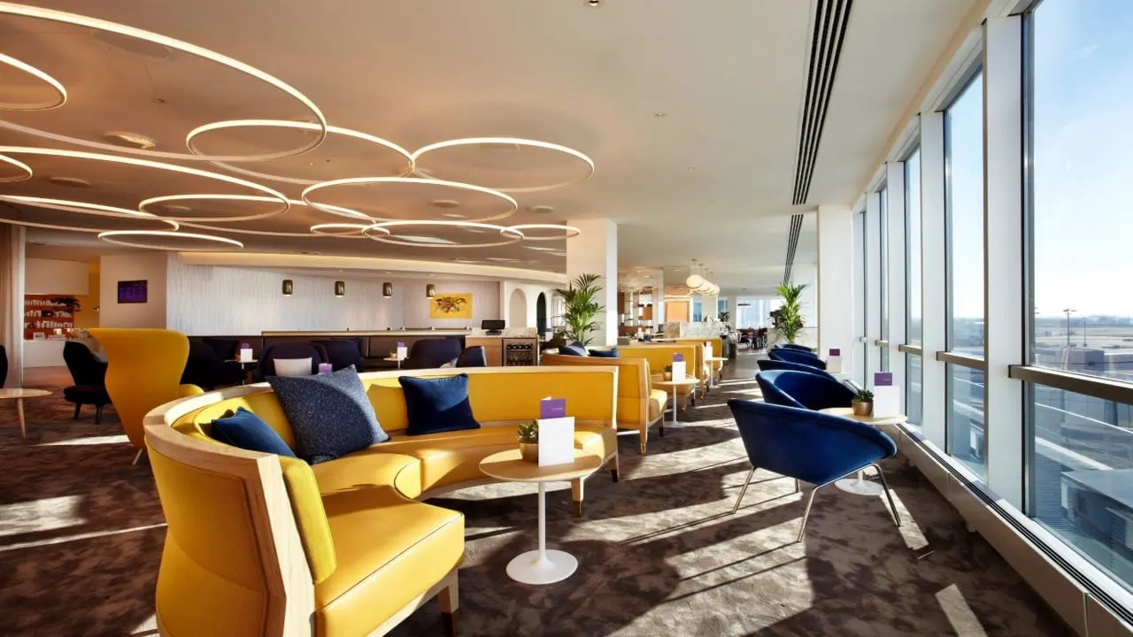 Mustard banquette with navy cushions and blue chairs along sunlit windows under circular ceiling lights
