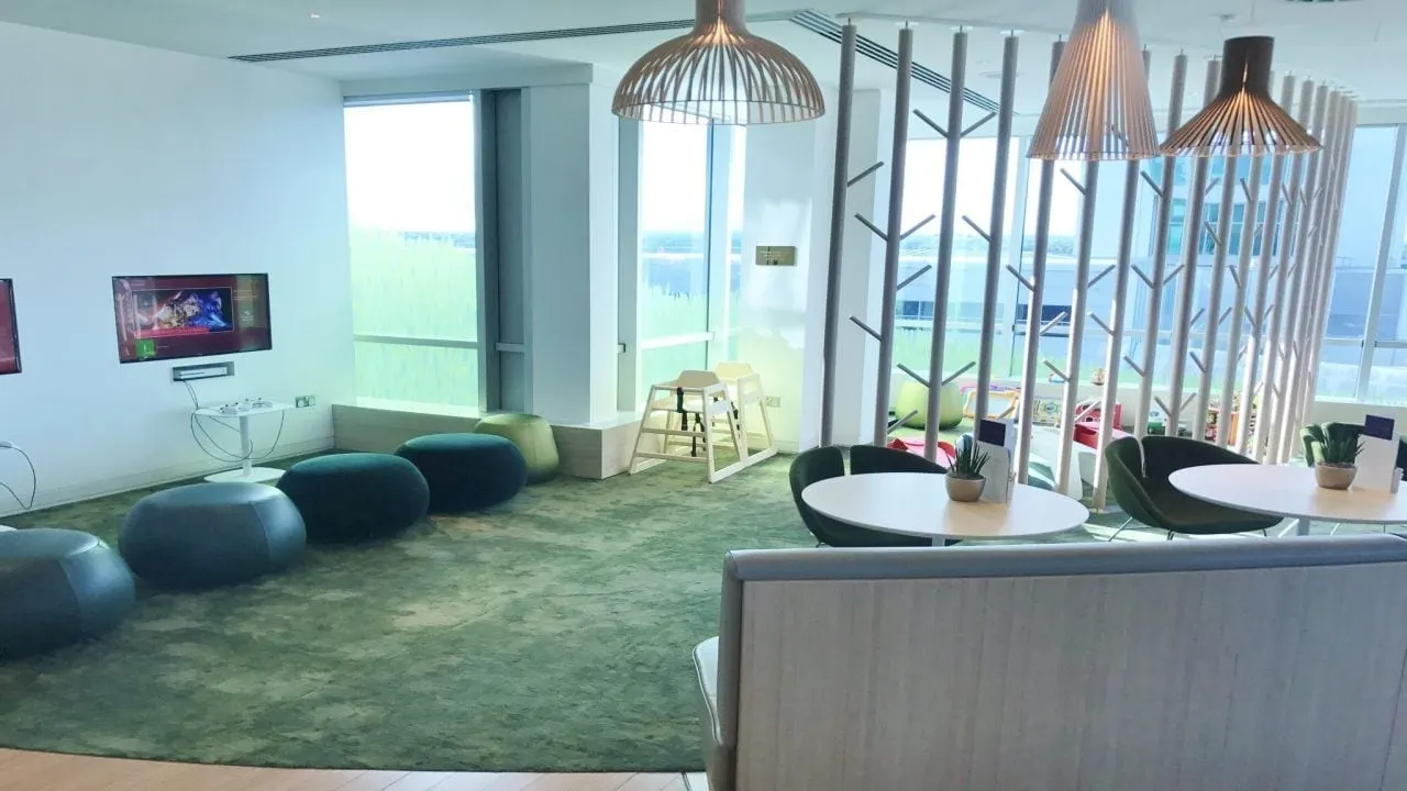 Children's play area with green carpet, soft seats and a wall TV beside the windows