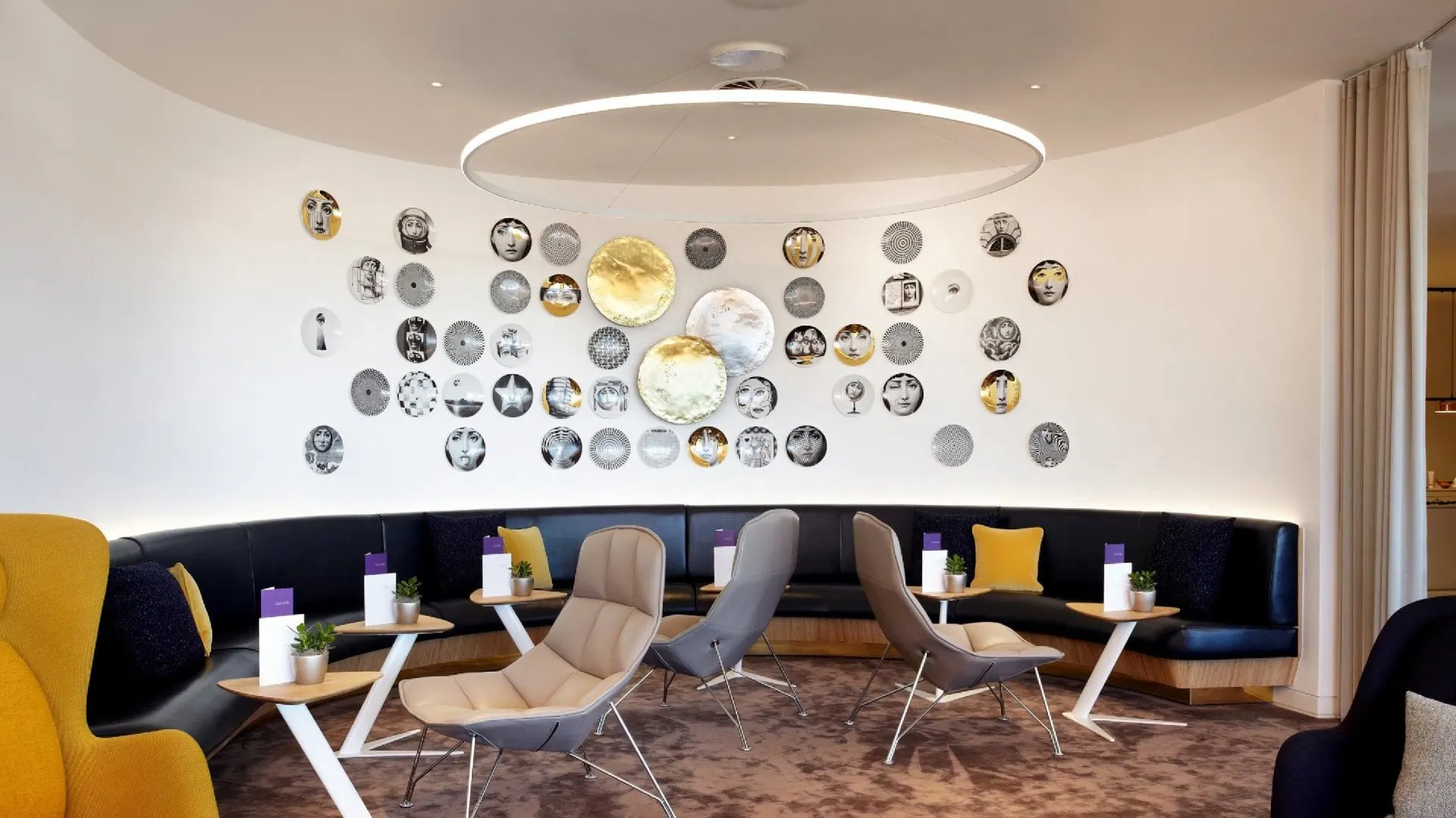 Curved navy banquette and grey armchairs below a wall decorated with plates