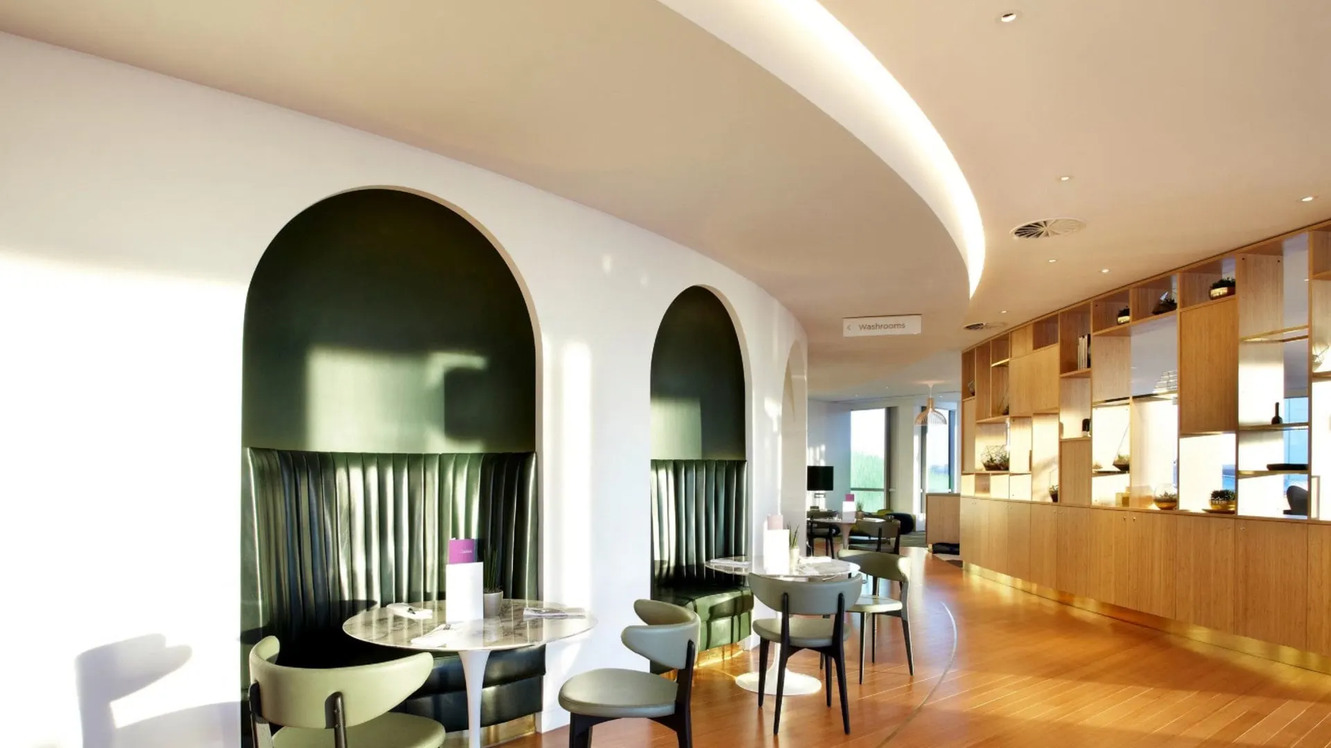 Two arched dark green alcoves with armchairs next to small café tables