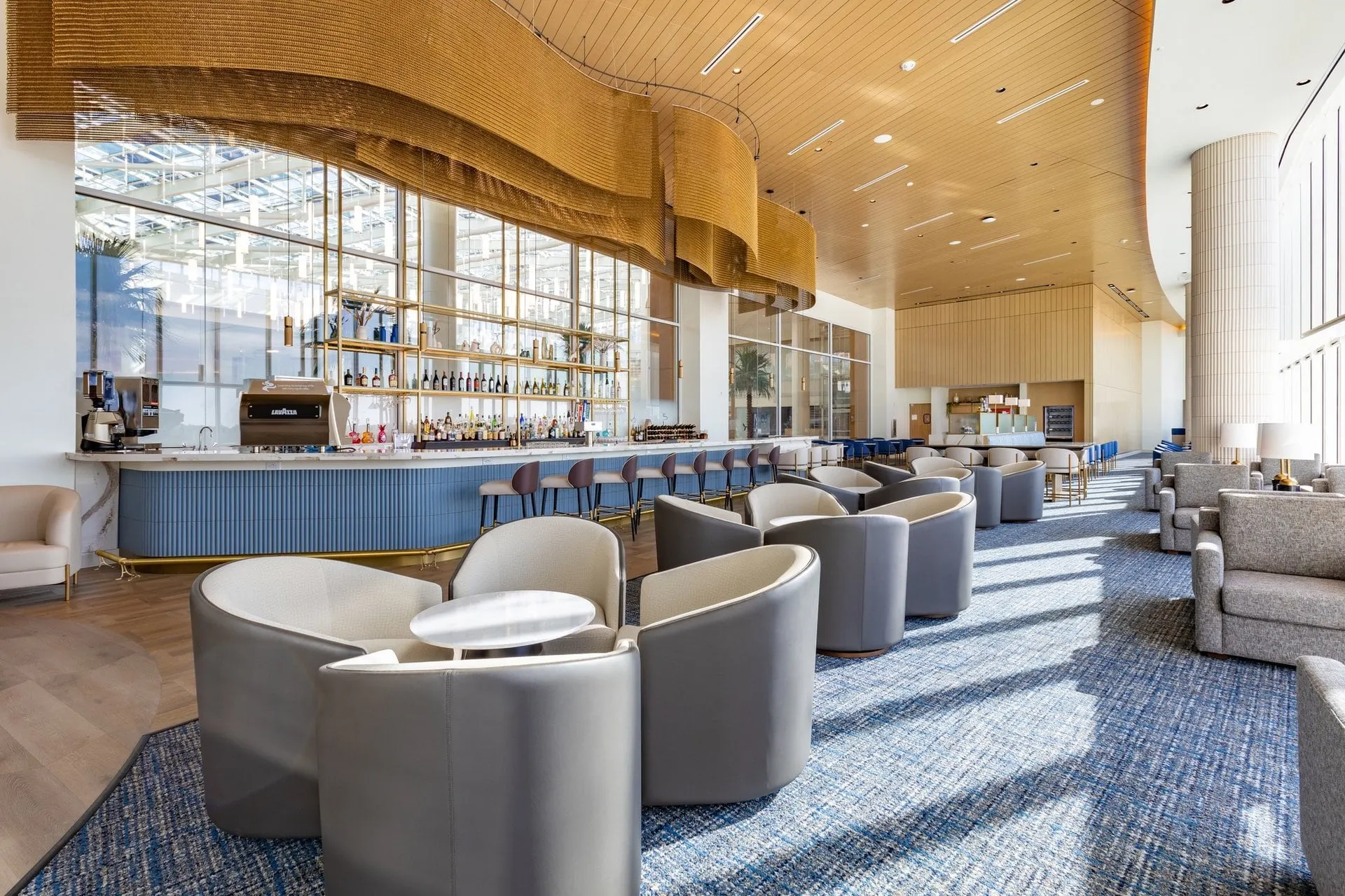 Lounge bar with a wave-shaped wooden ceiling, curved grey armchairs and floor-to-ceiling windows