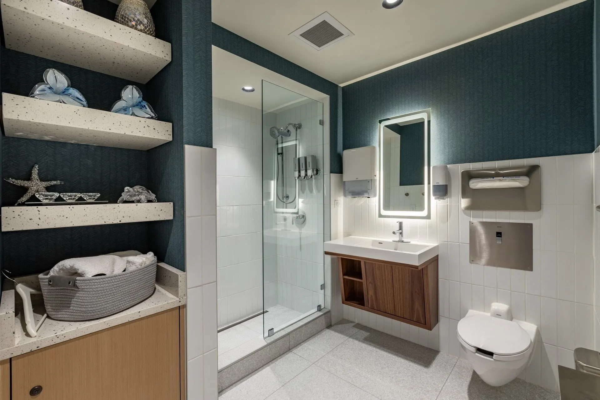 Shower room with a glass walk-in shower, a lit mirror and shelves of towels