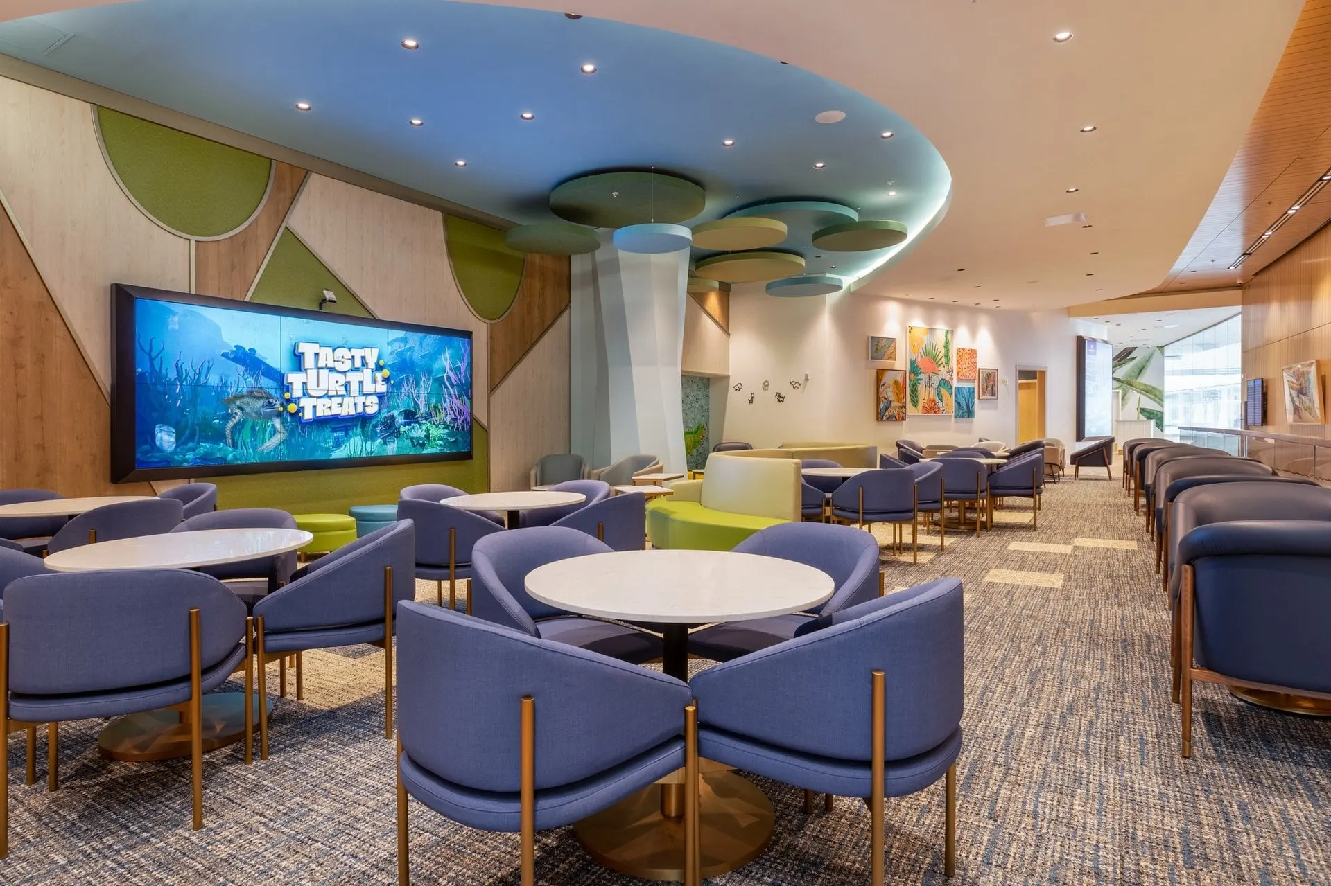 Family dining area with purple chairs, round tables and a big screen showing a sea scene