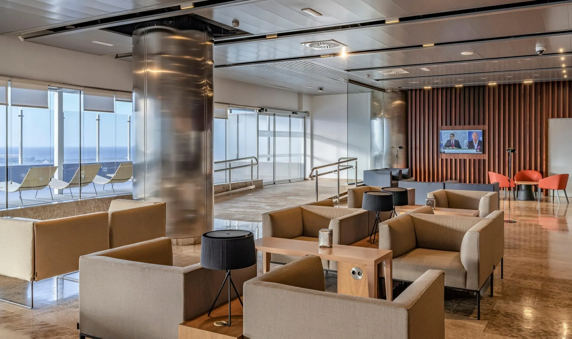 Beige armchairs and low tables by tall windows looking out to the ocean in the Galdós lounge