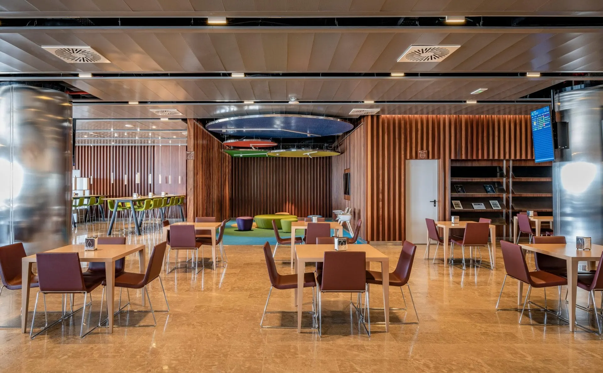 Wooden dining tables with purple chairs, a bookshelf and a colourful children's corner at the back