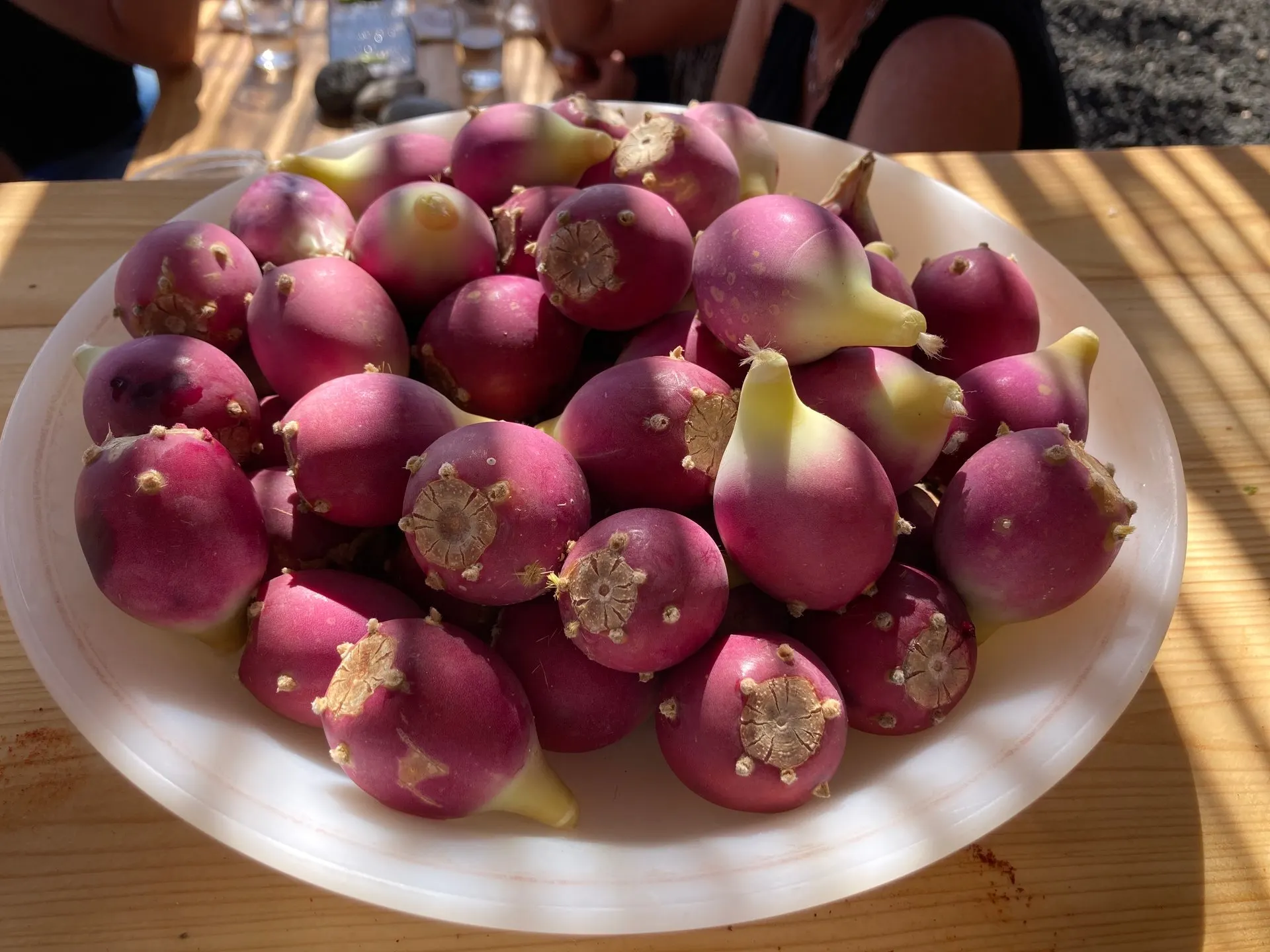A bowl of pink prickly pears, the cactus fruit, on a wooden table in the sun