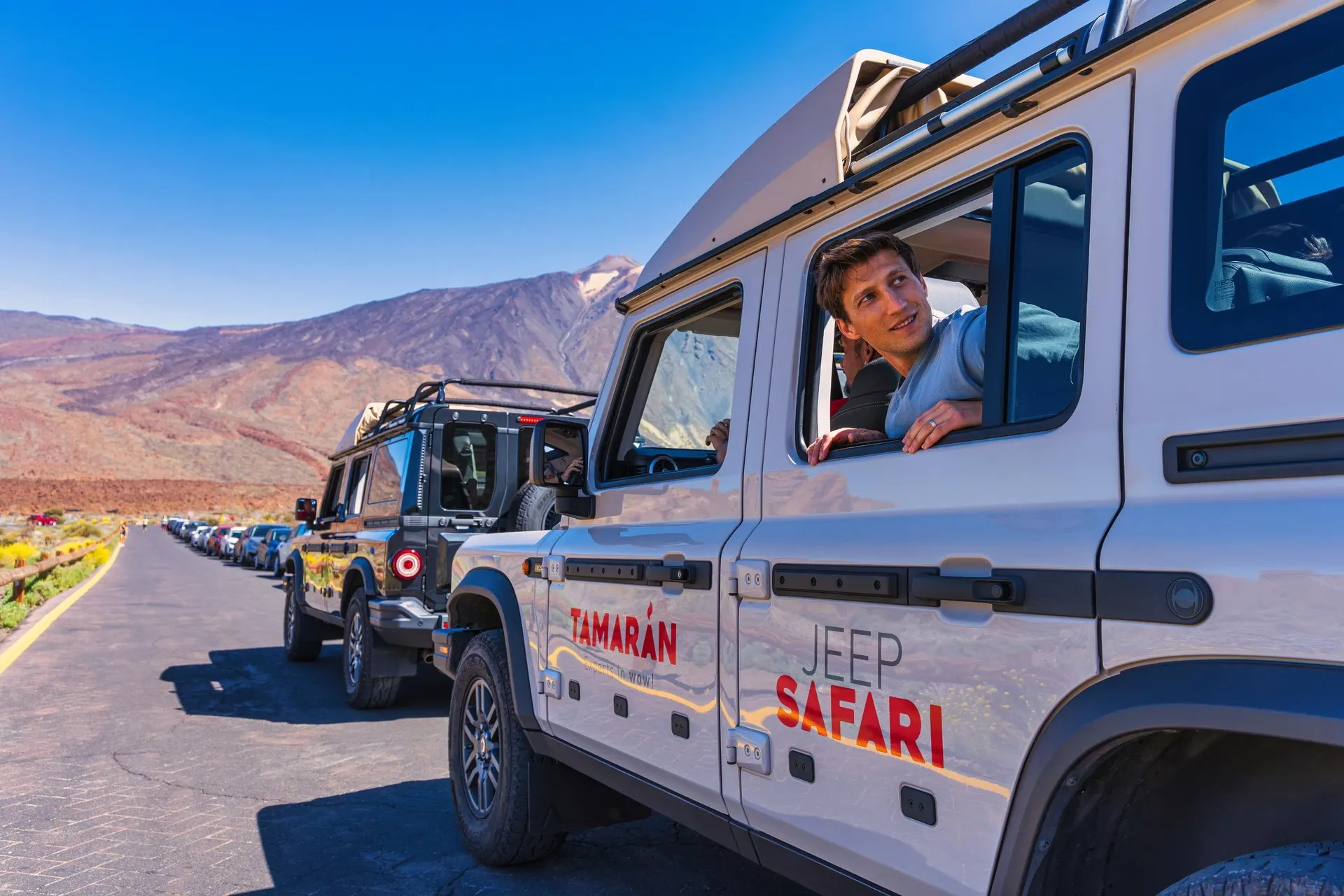 A line of jeeps on a road in Teide National Park, with the volcano behind