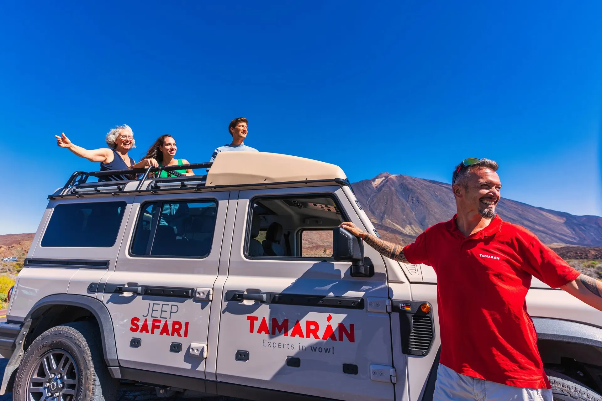 The guide beside a jeep as passengers wave from the roof