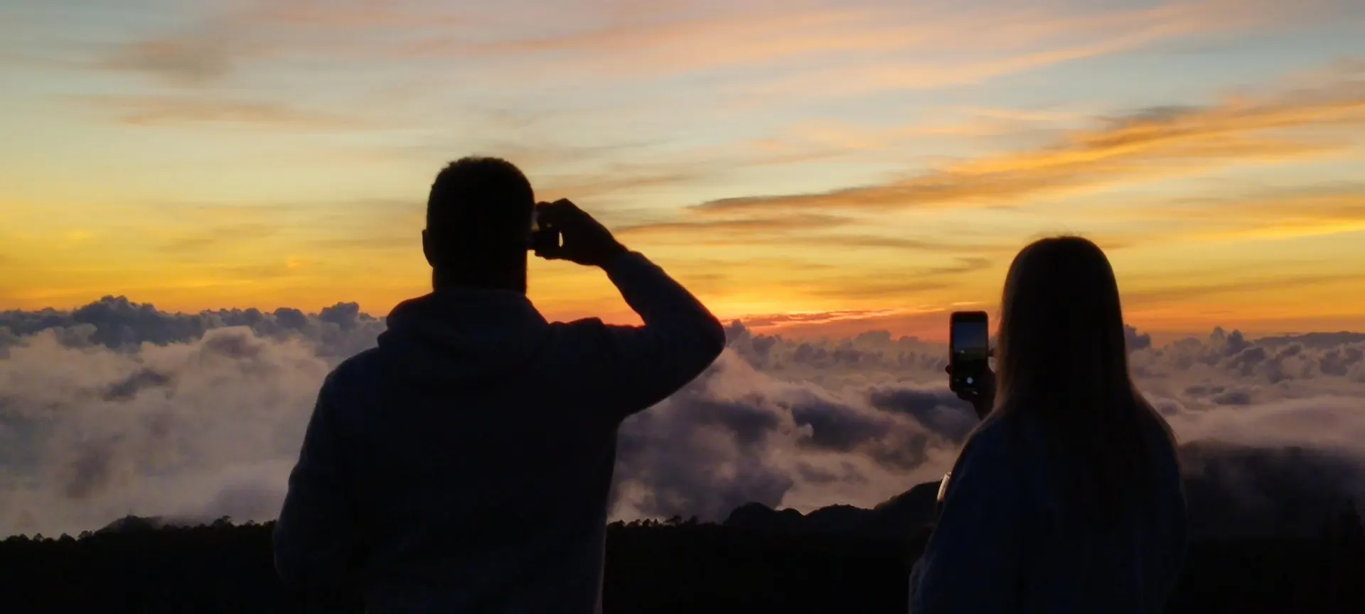 Due visitatori fotografano il tramonto sopra il mare di nuvole dai pendii del Teide