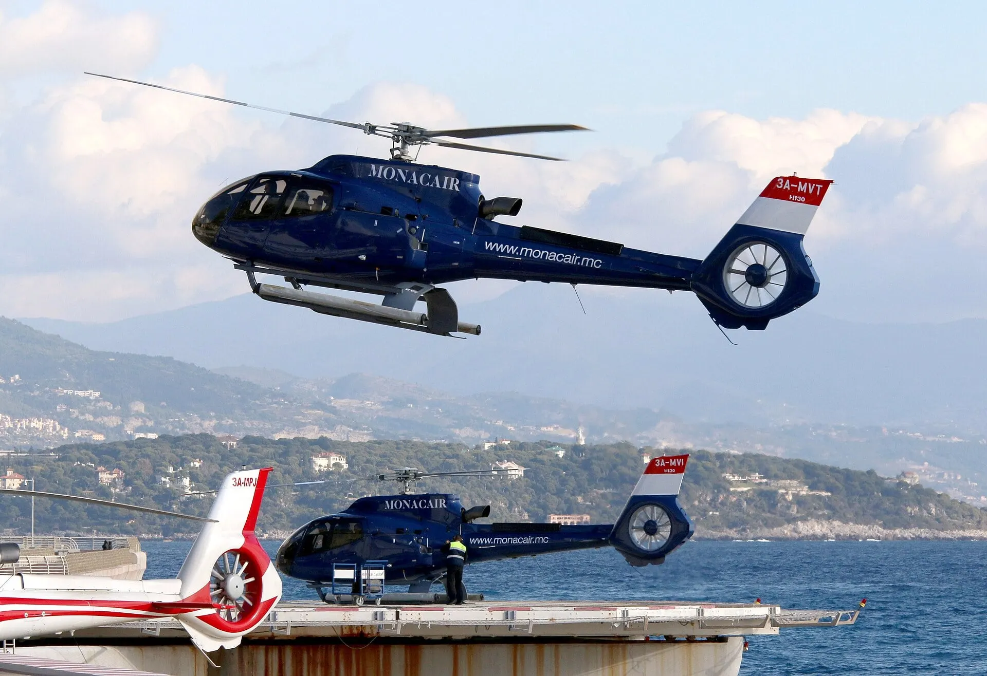 Helicopters on the pads at the Monaco heliport, with the coast towards Nice behind