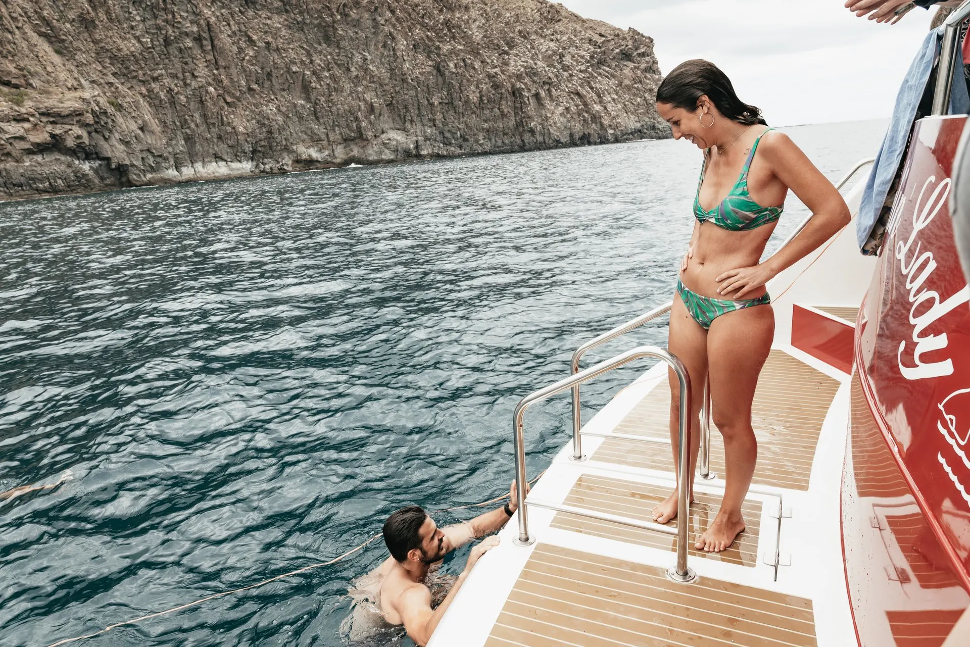 A swimmer on the stern steps of the yacht at the swim stop, by the cliffs