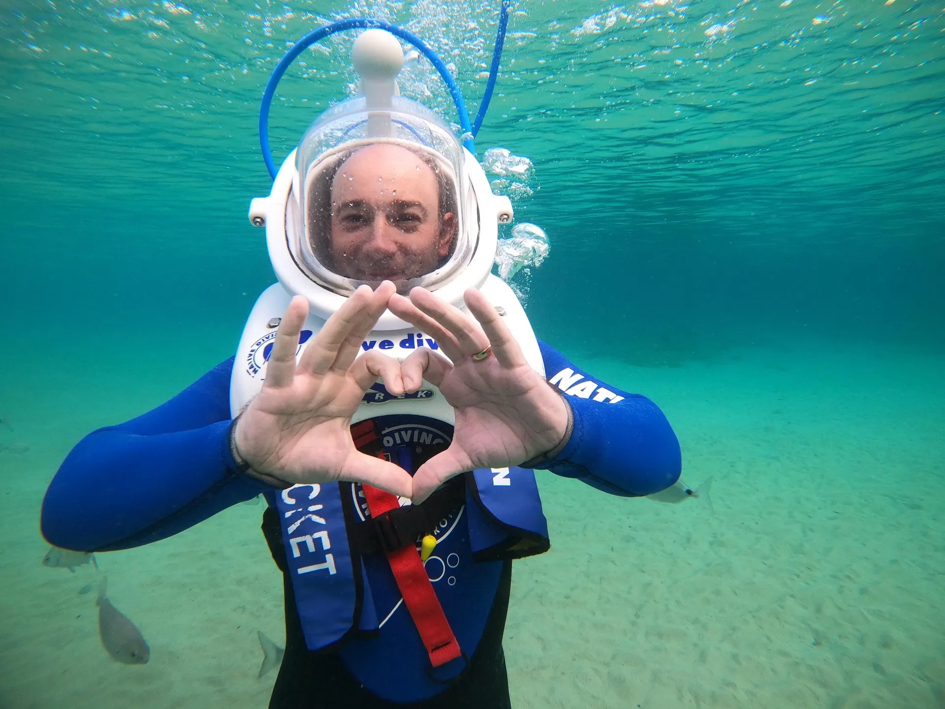 A smiling walker in a Sea Trek helmet, with air bubbles rising above