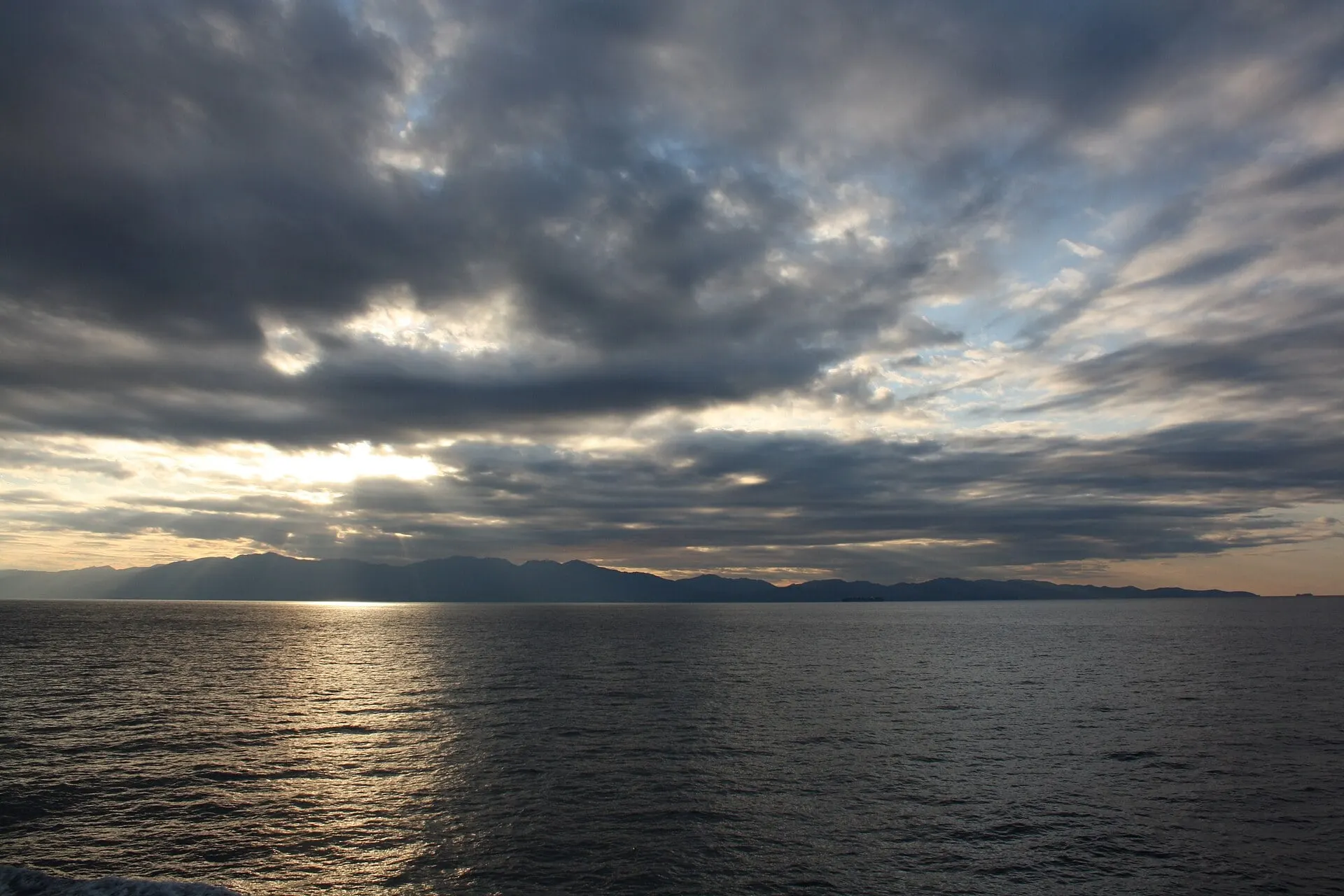 The mountains of Cap Corse seen from the sea under a clouded sky, with sunlight on the water