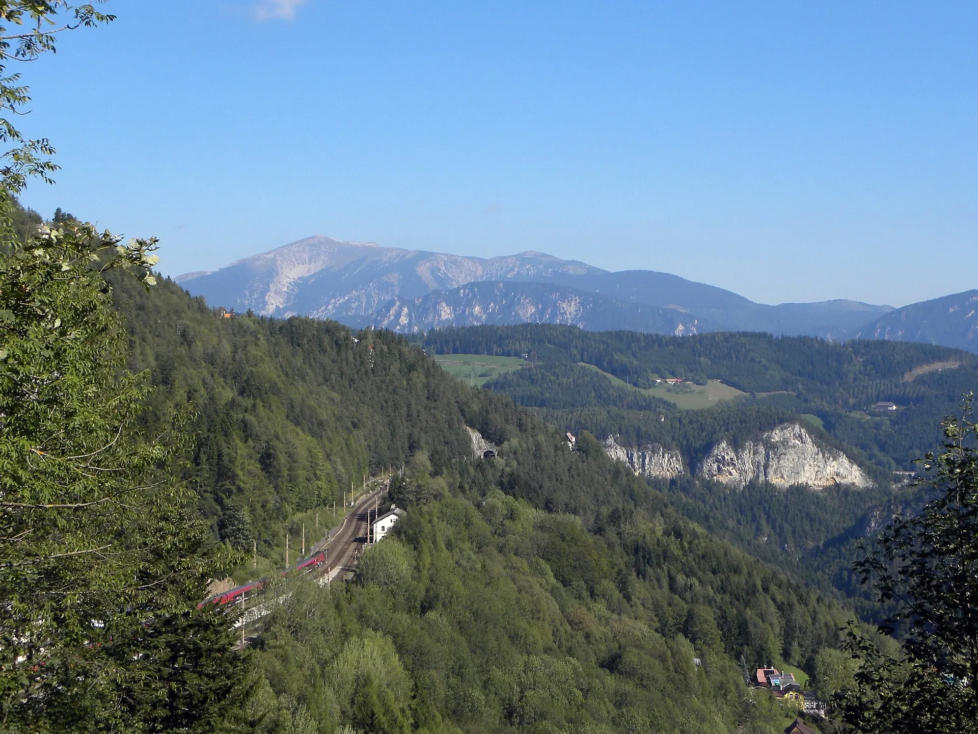 The Semmering Railway winding along a forested slope near Semmering, with the Schneeberg on the horizon