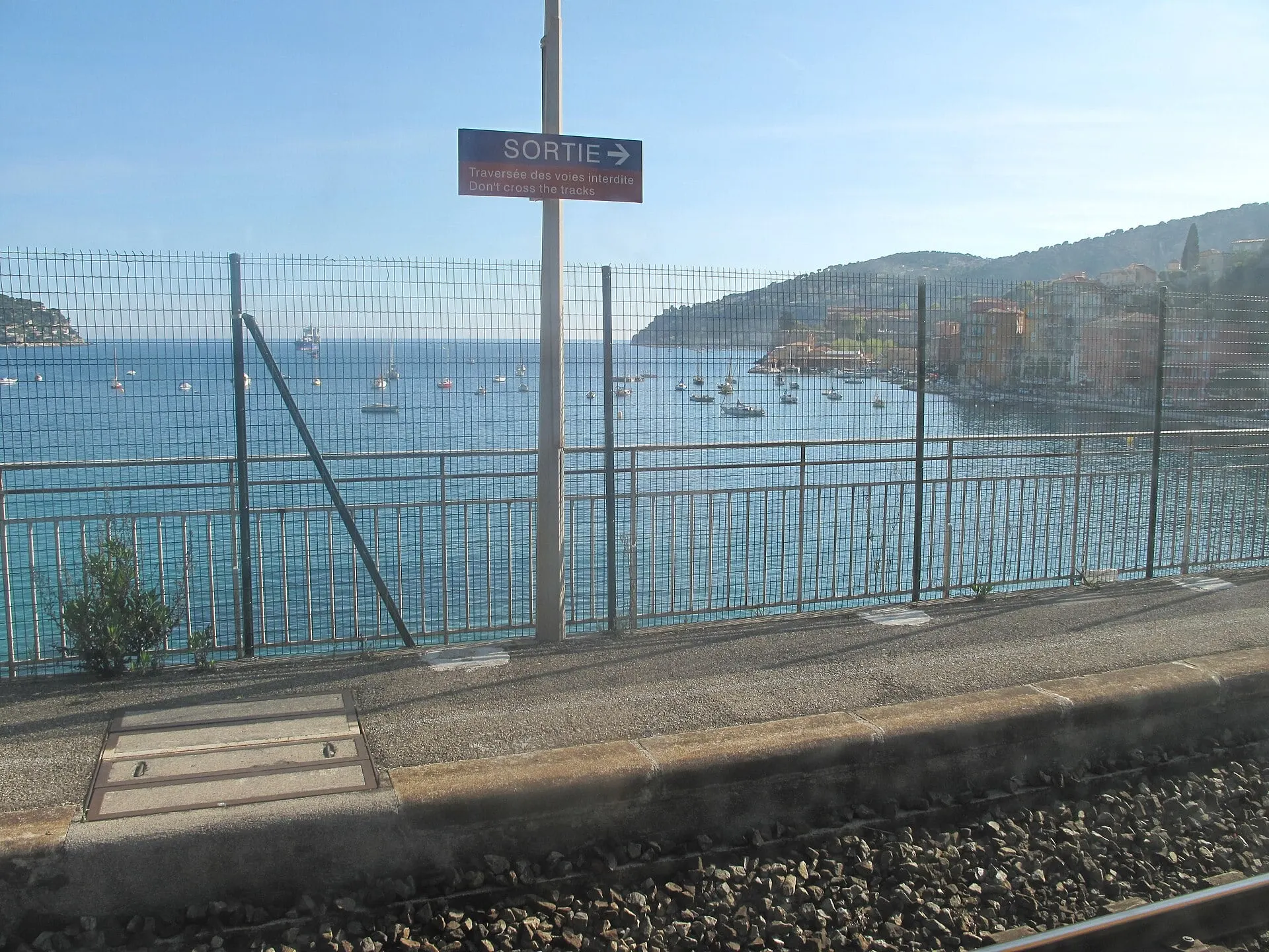 The bay of Villefranche and Cap Ferrat seen across the railings of the station platform.