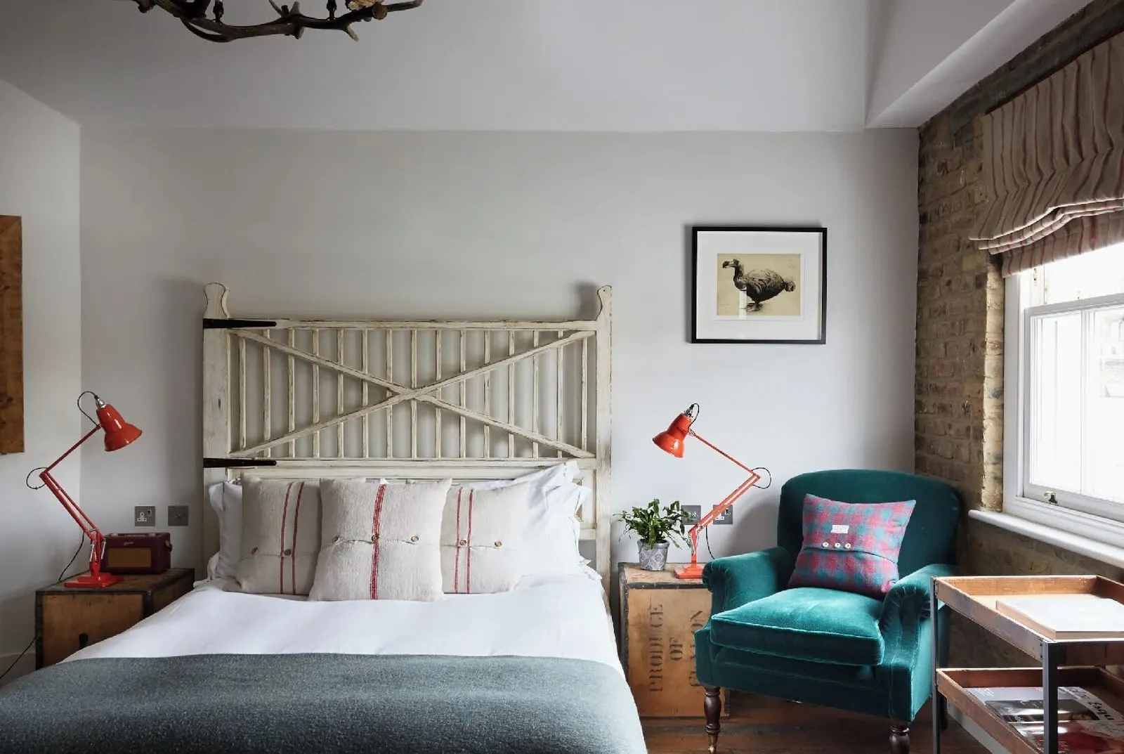 The Loft at Artist Residence London: the bed with a wooden gate headboard, red lamps and a teal velvet armchair