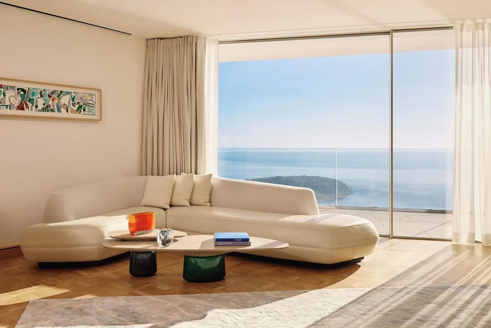 Sea View Suite at The Maybourne Riviera: the living room with a long curved sofa facing a wall of glass onto the sea
