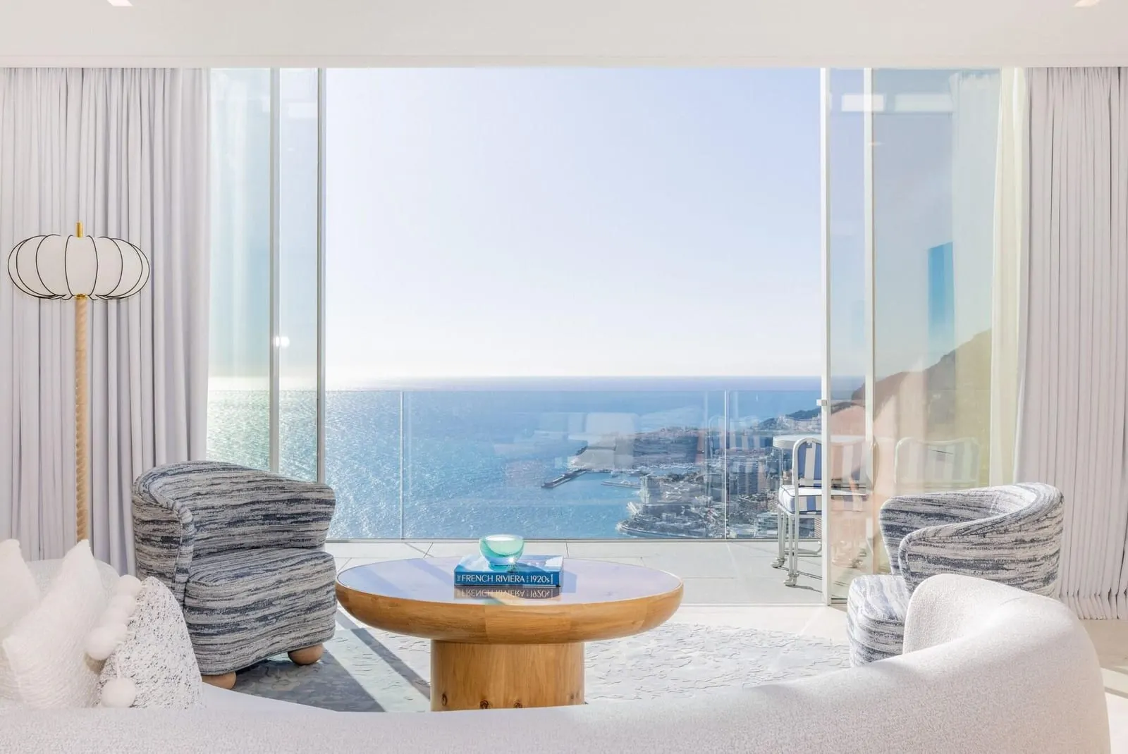 The Azur Suite at The Maybourne Riviera: armchairs and a round table before a wall of glass onto the sea and the coast